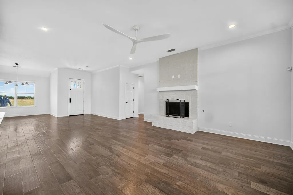 Spacious living area featuring wood-finish flooring, a white brick fireplace with a mantel, and recessed lighting