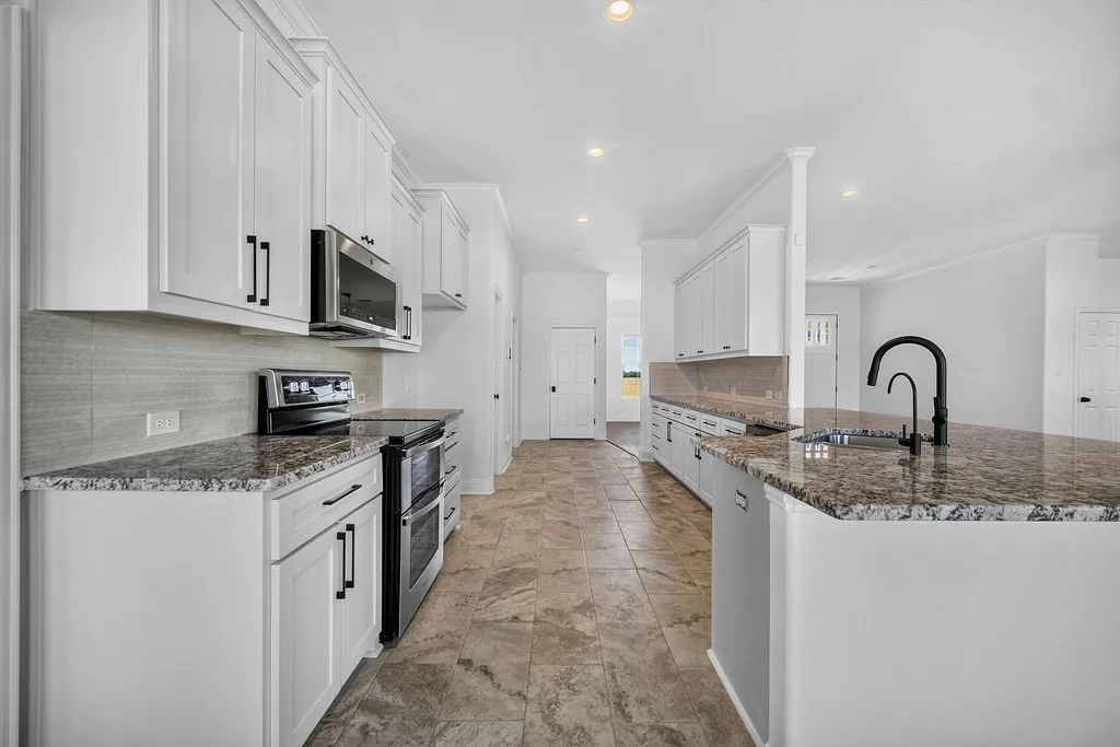 White shaker cabinetry with black hardware, stainless steel appliances, speckled countertops, tile flooring, and a large center island with an undermount sink