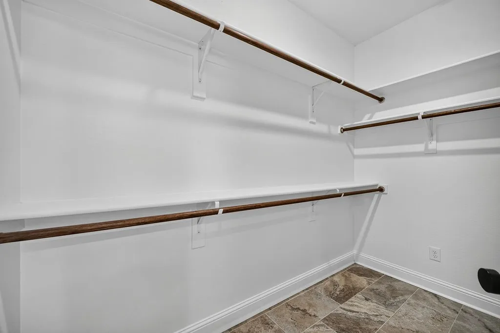 Walk-in closet with multiple hanging rods, shelving, and textured tile flooring