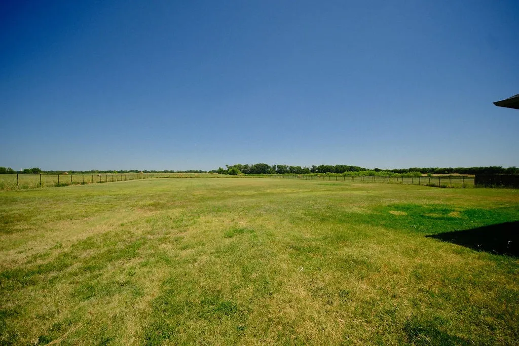 Expansive green lawn with perimeter fencing and distant tree line