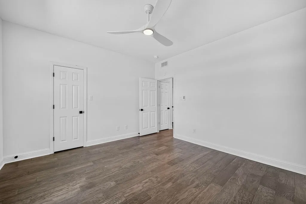 White walls, wood-finish flooring, contemporary ceiling fan with integrated lighting, and multiple paneled doors