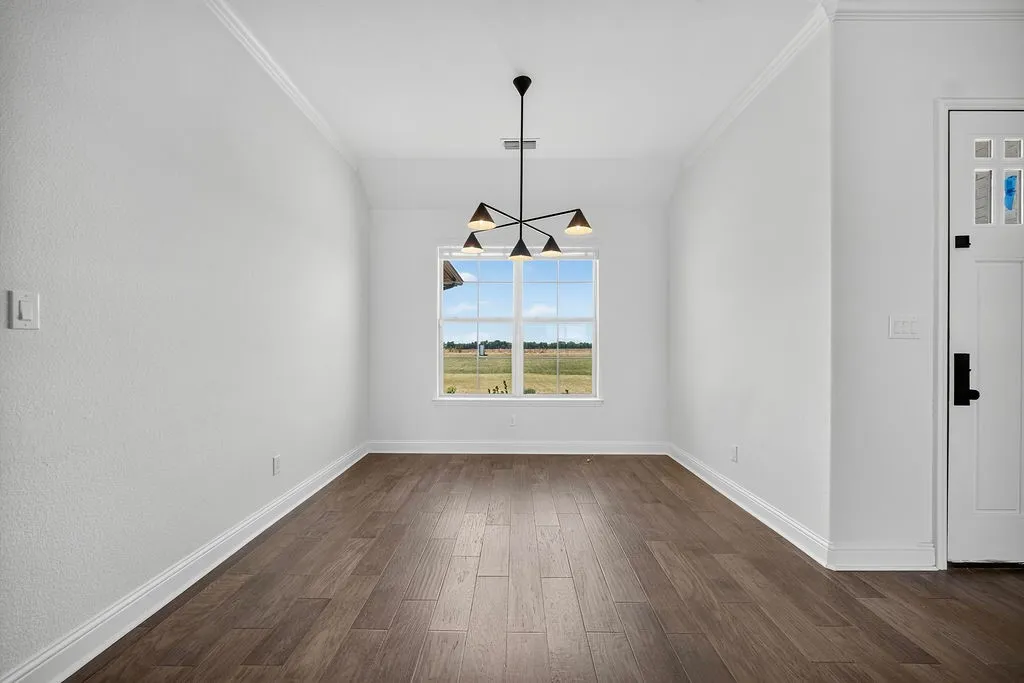 Wood-finish flooring with crisp white baseboards, crown molding, and a contemporary chandelier