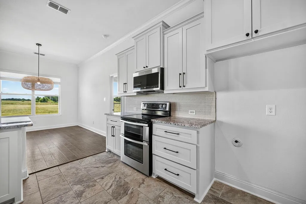 White shaker-style cabinetry with matte black hardware, stainless steel appliances, tile flooring, and a stone-finish countertop