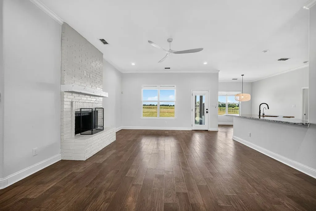 Spacious room featuring wood-finish flooring, a painted brick fireplace, recessed lighting, and a ceiling fan