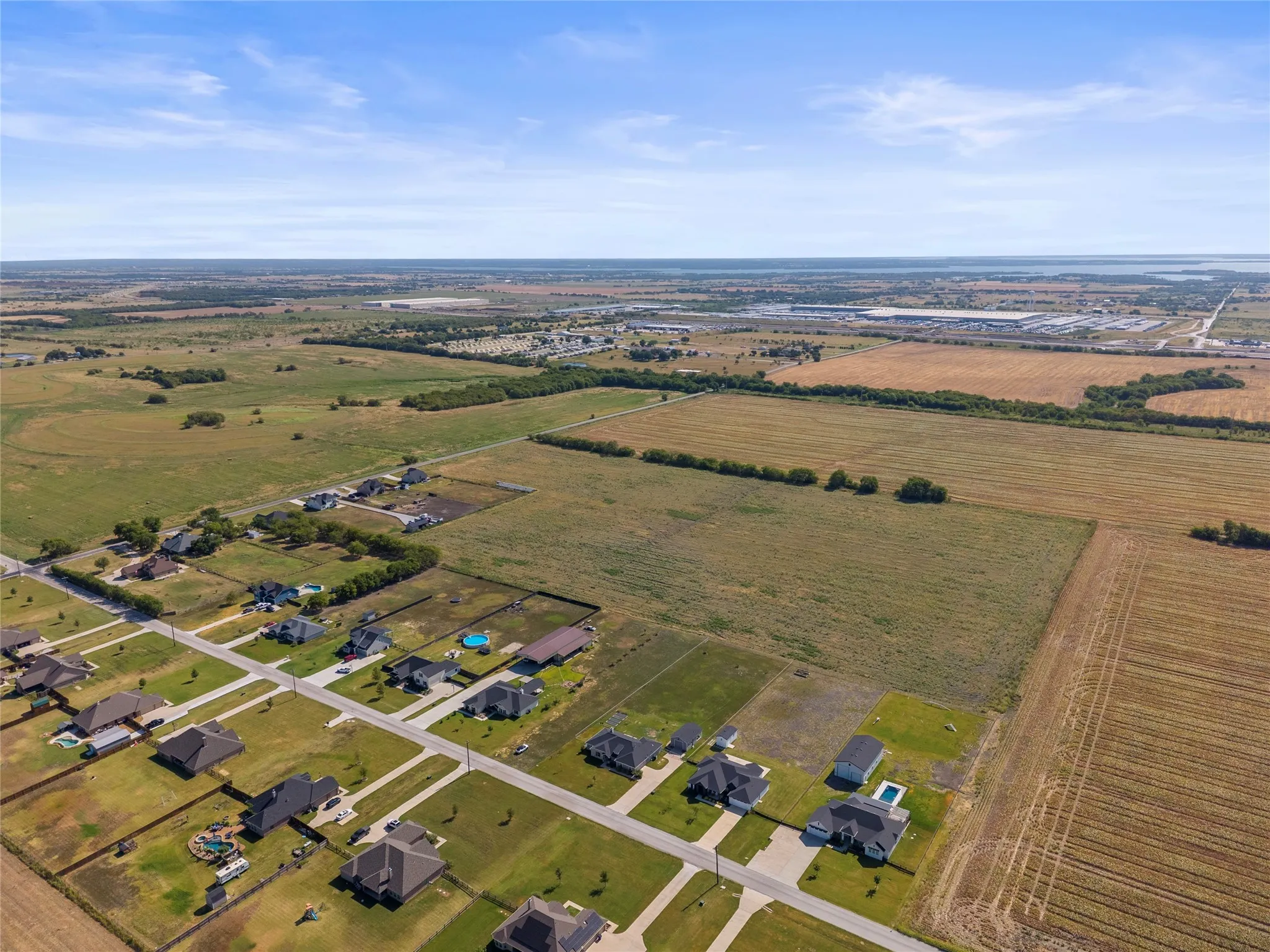 Expansive land parcel featuring open fields and established residential areas, with a distant body of water