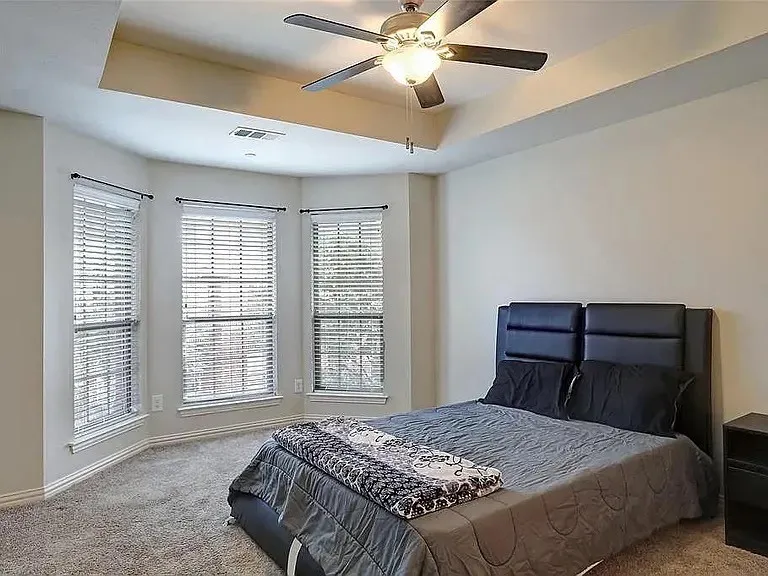 Carpeted bedroom featuring visible vents, baseboards, a tray ceiling, and a ceiling fan
