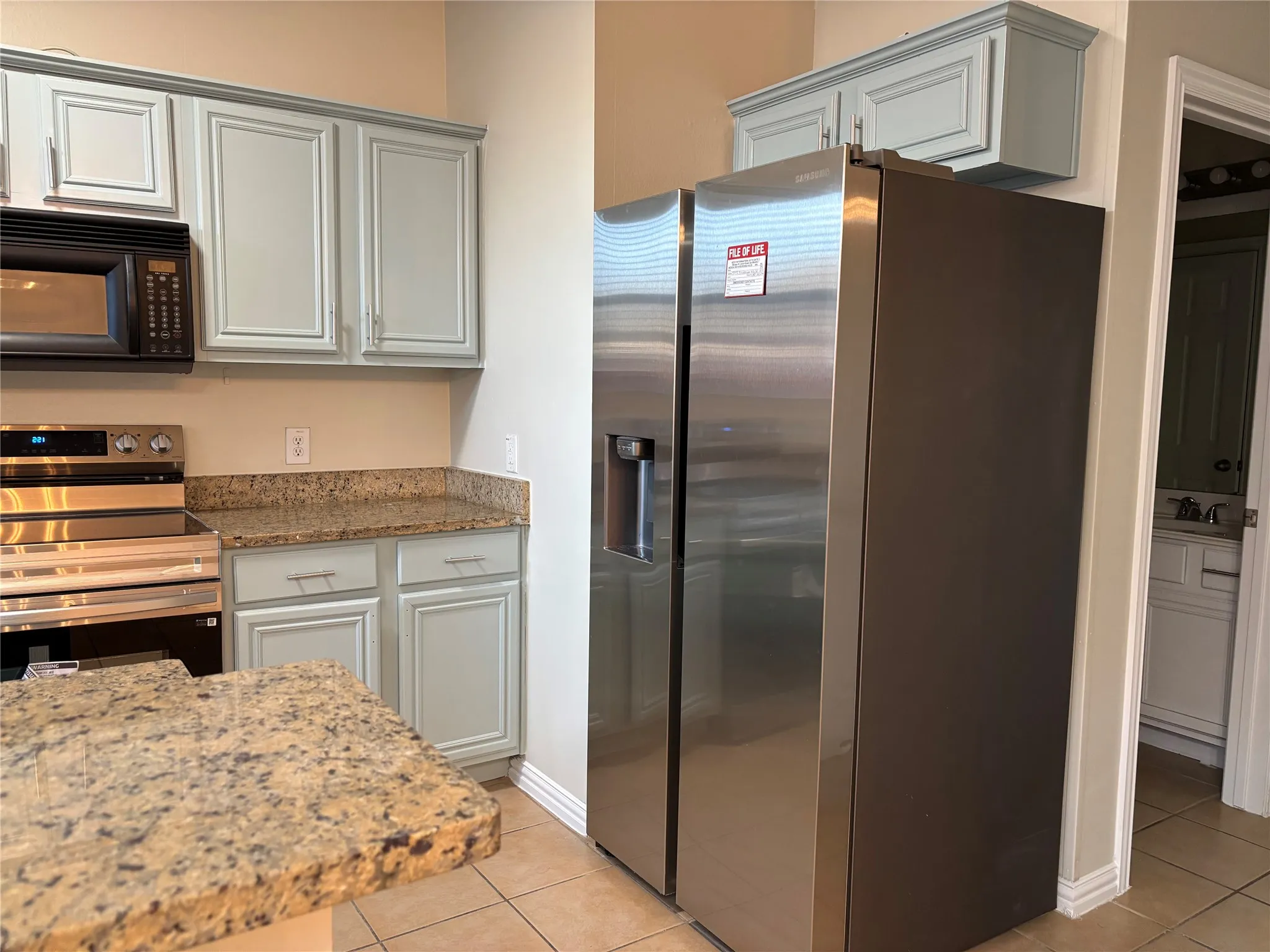 Kitchen with light stone countertops, baseboards, light tile patterned flooring, a sink, and appliances with stainless steel finishes