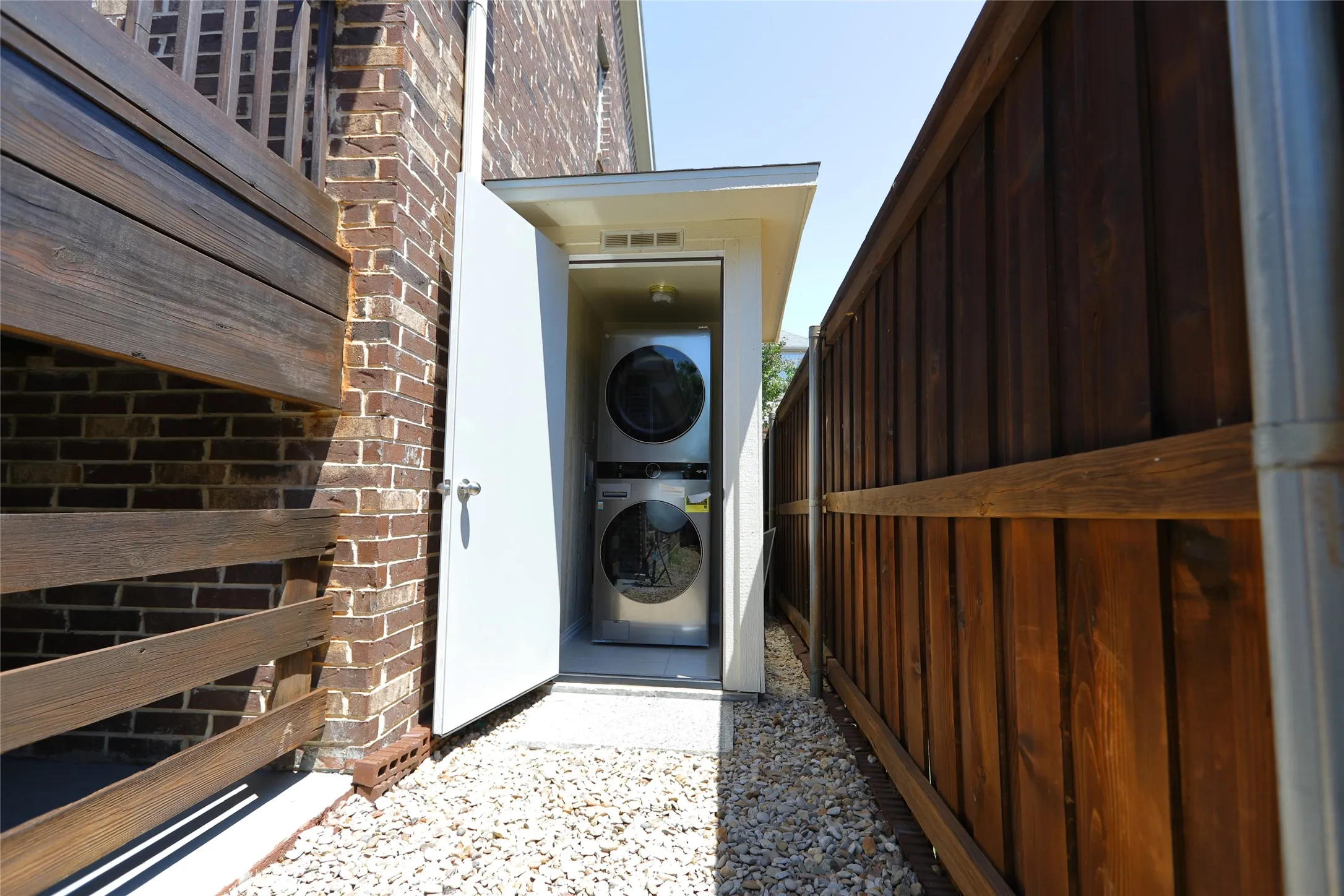 Enclosed laundry area featuring a stacked washer and dryer unit, set on a gravel pathway