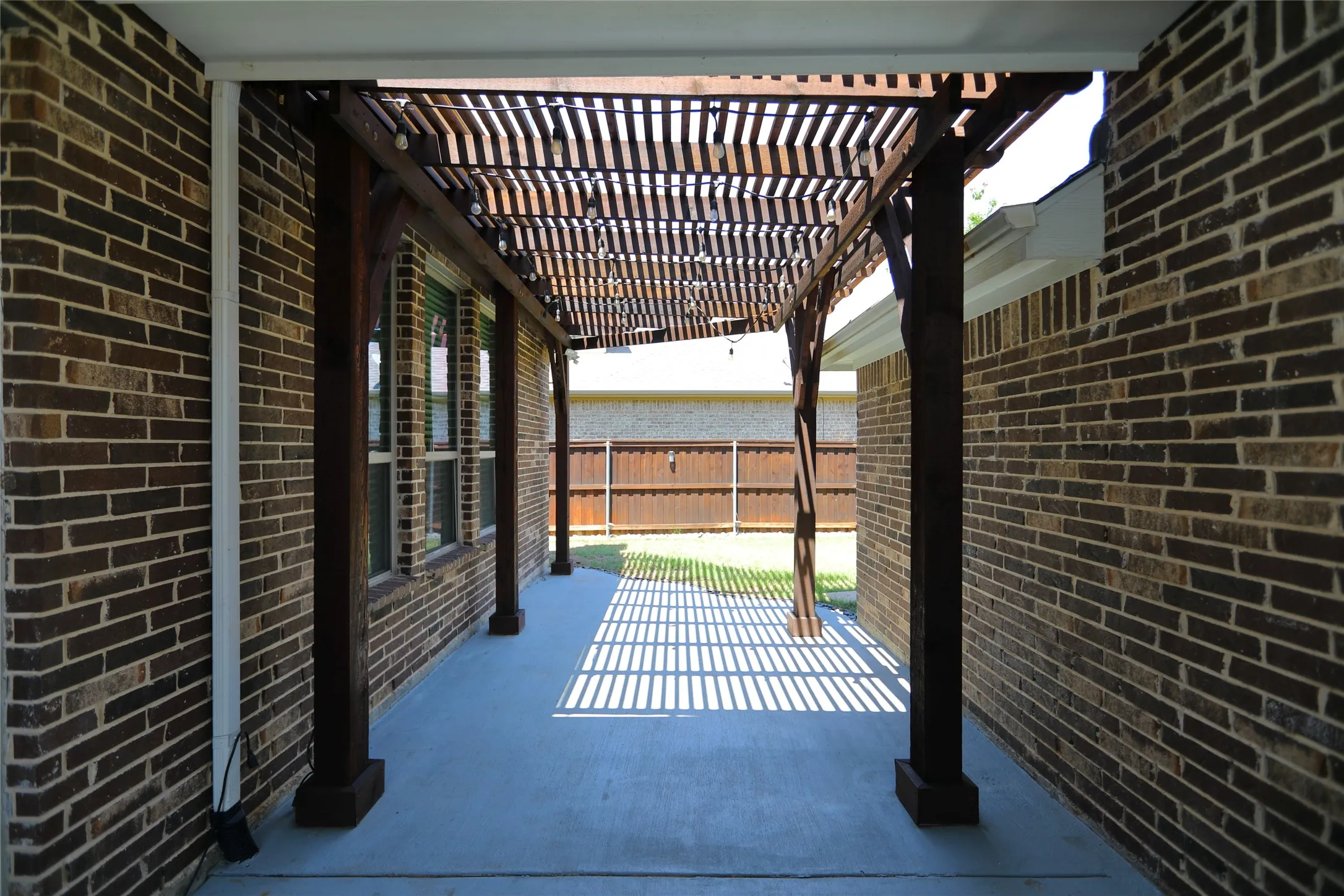Covered patio featuring a wood pergola with slatted roof, concrete flooring, and brick exterior walls