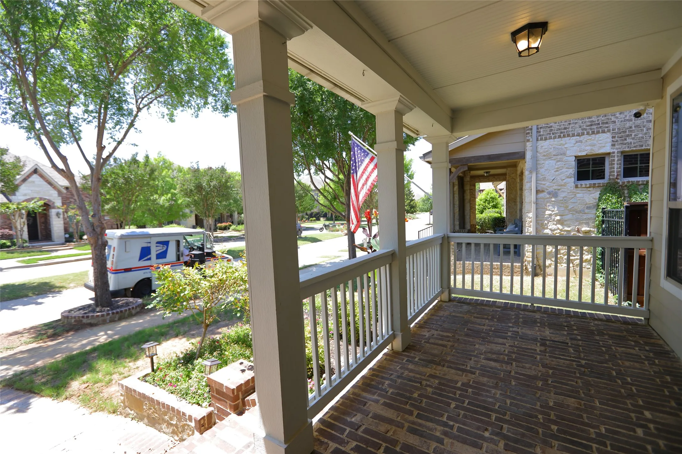 Brick-paved front porch featuring white painted railings, substantial support columns, a beadboard ceiling, and a mounted outdoor light fixture