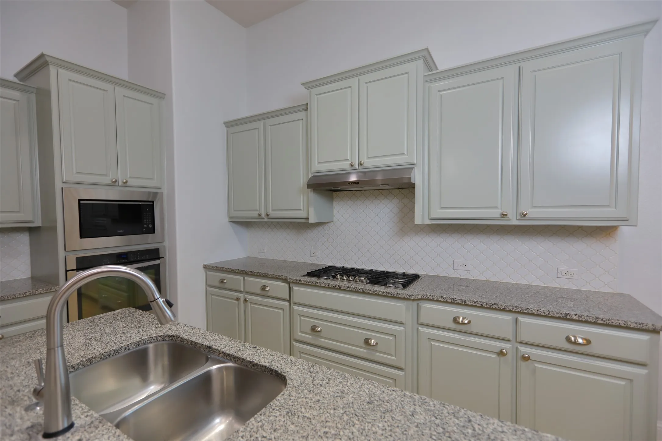 Kitchen featuring light grey cabinetry, stainless steel appliances, a gas cooktop, white tile backsplash with a diamond pattern, and granite countertops