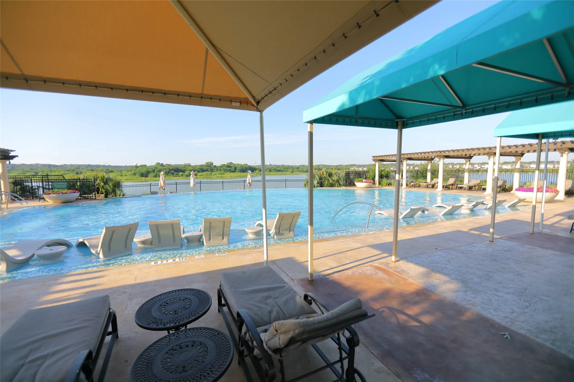 Expansive infinity-edge pool surrounded by a concrete deck with multiple shade structures