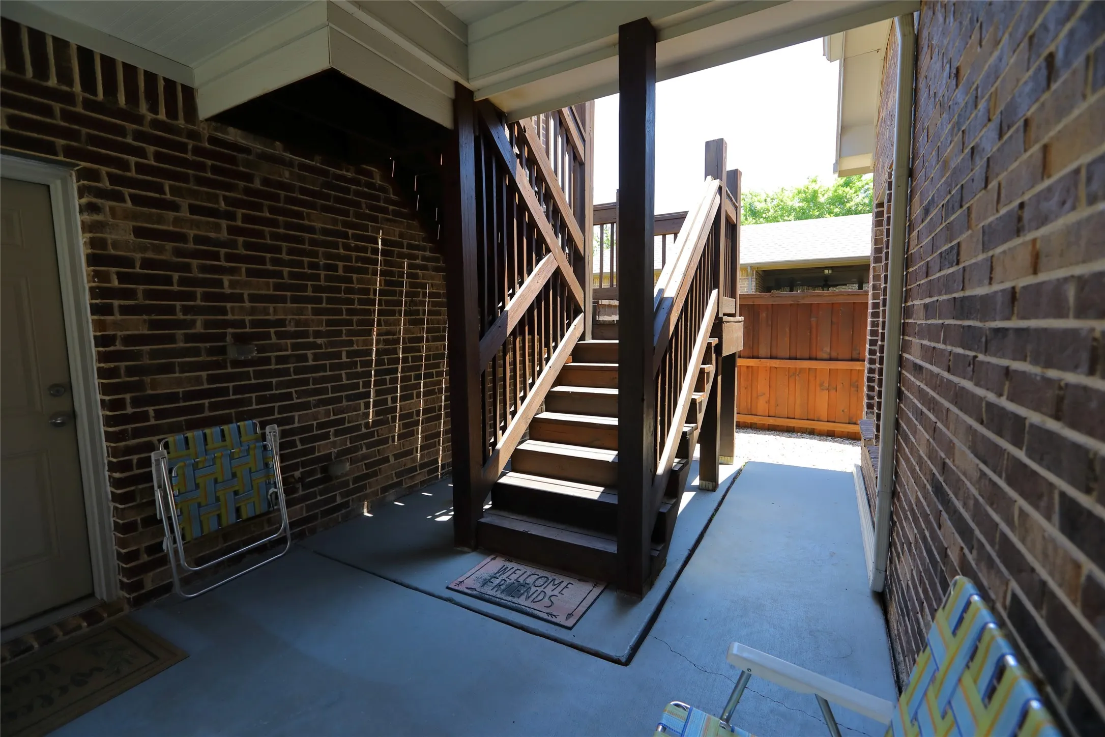 Covered outdoor walkway featuring a wooden staircase, brick wall, and concrete flooring