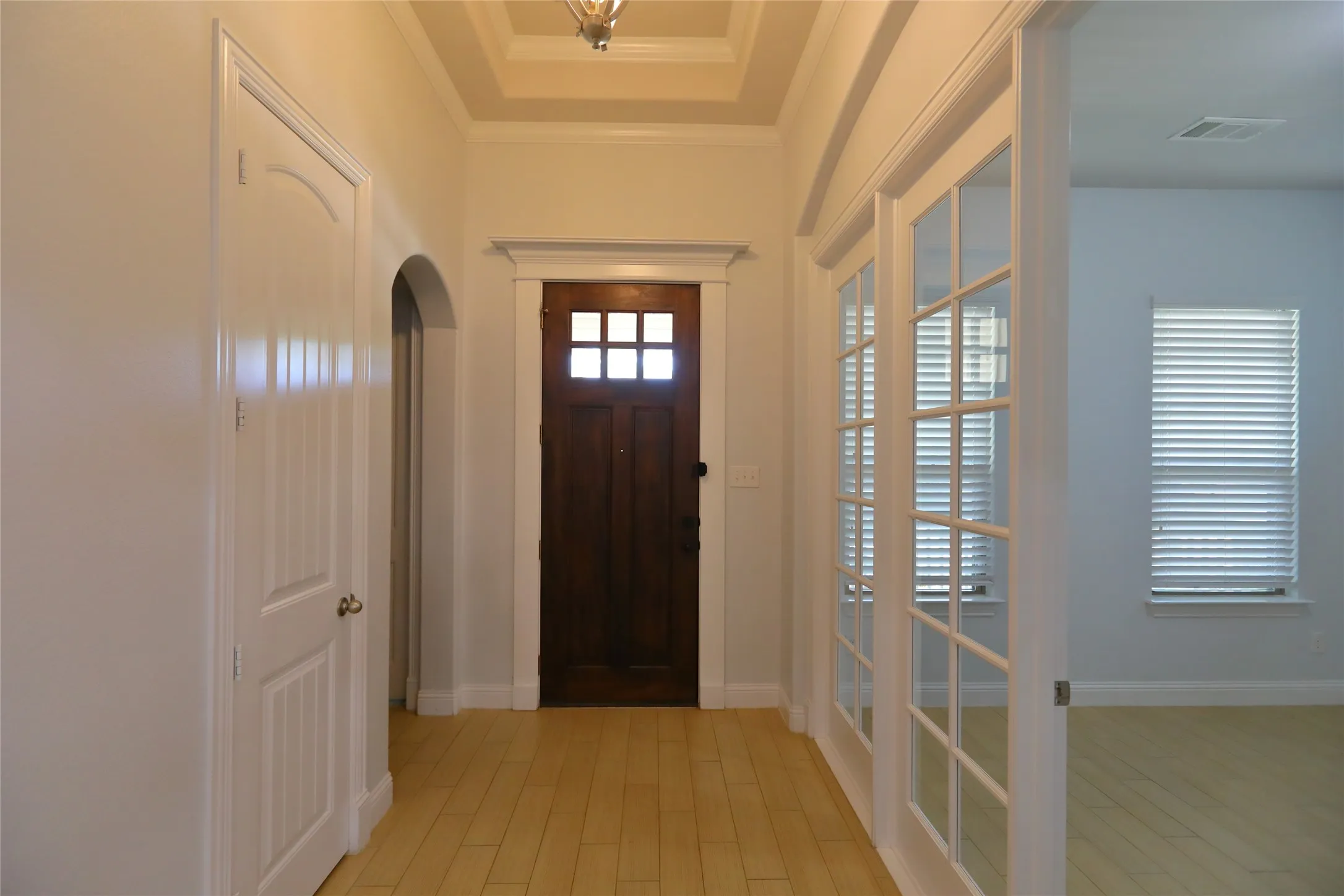 Entryway featuring light wood-finish flooring, a dark wood front door with glass panes, white paneled interior doors, an arched doorway, and French doors with multiple glass lites