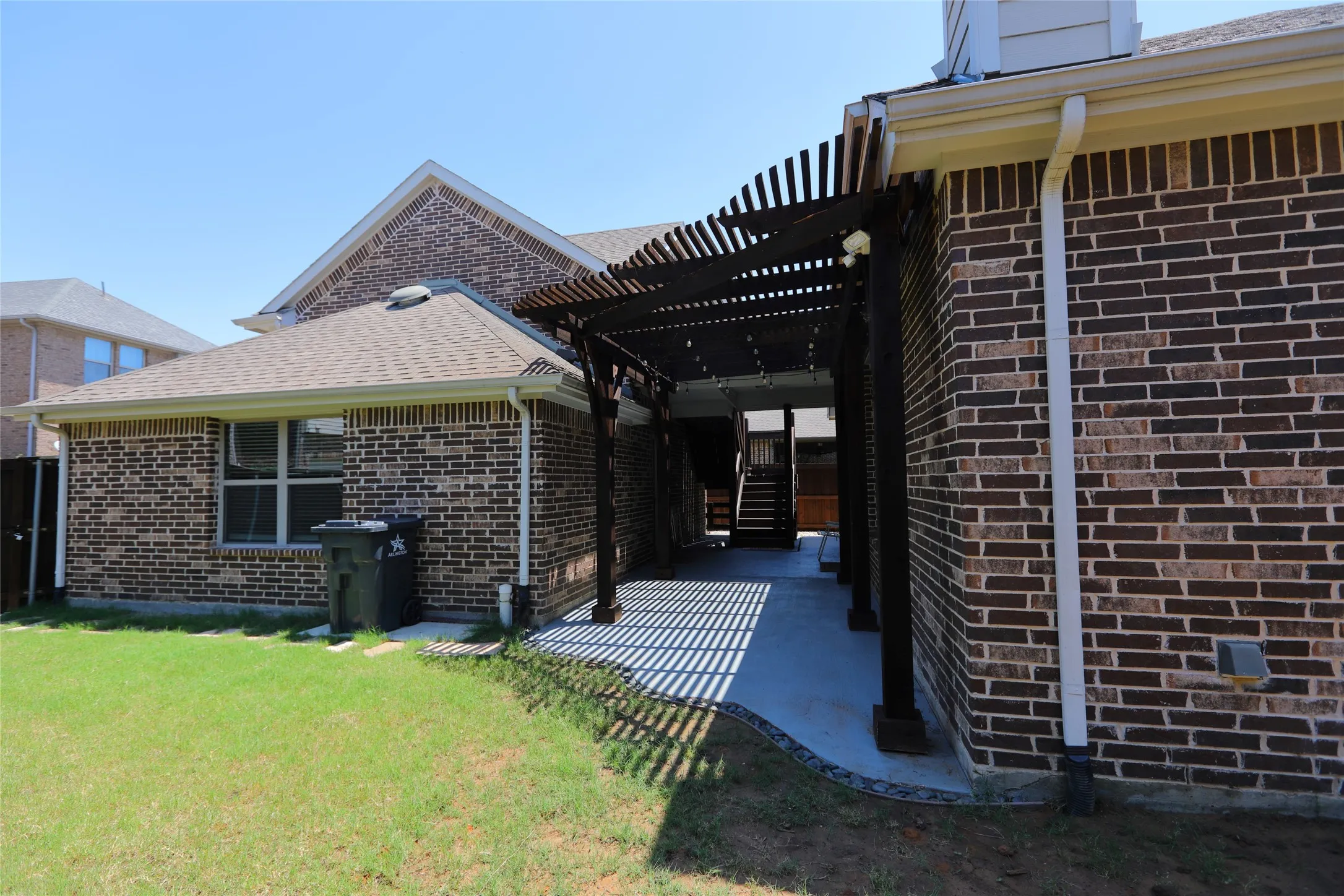 Brick exterior with a covered patio featuring a dark wood pergola