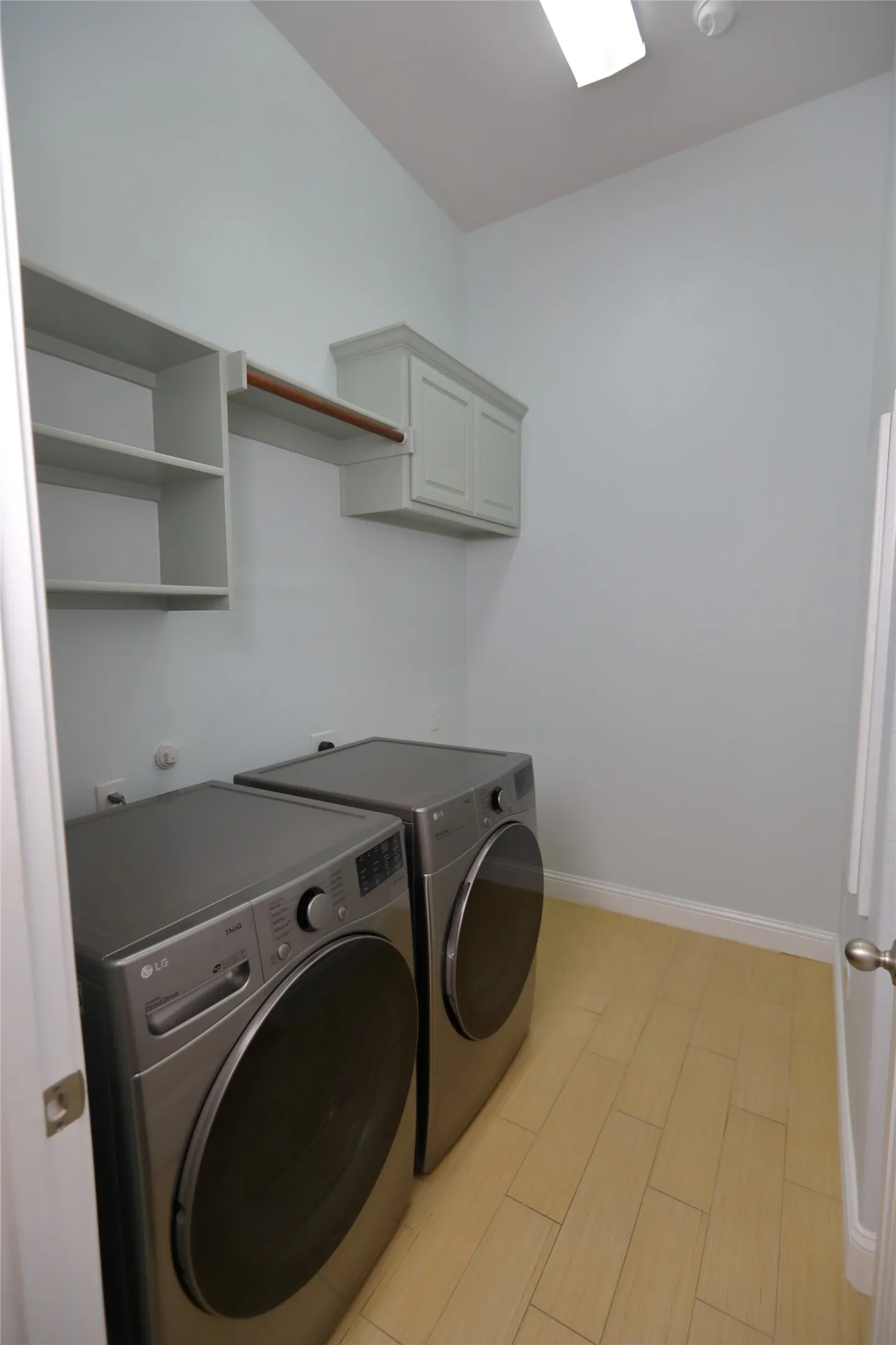 Dedicated laundry room featuring light wood-finish flooring, built-in open shelving, an integrated hanging rod, and a built-in upper cabinet