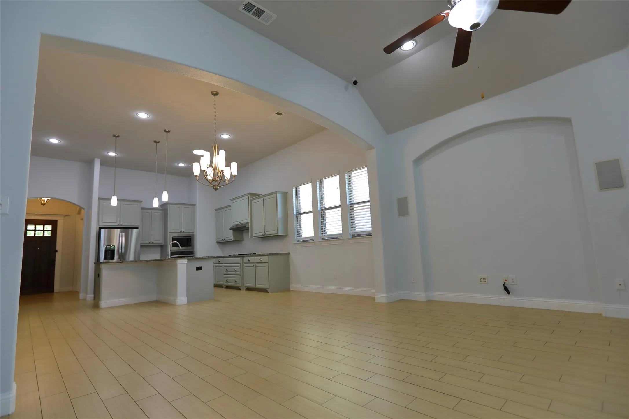 Open-concept living area featuring light wood-finish flooring, a vaulted ceiling, and an arched niche