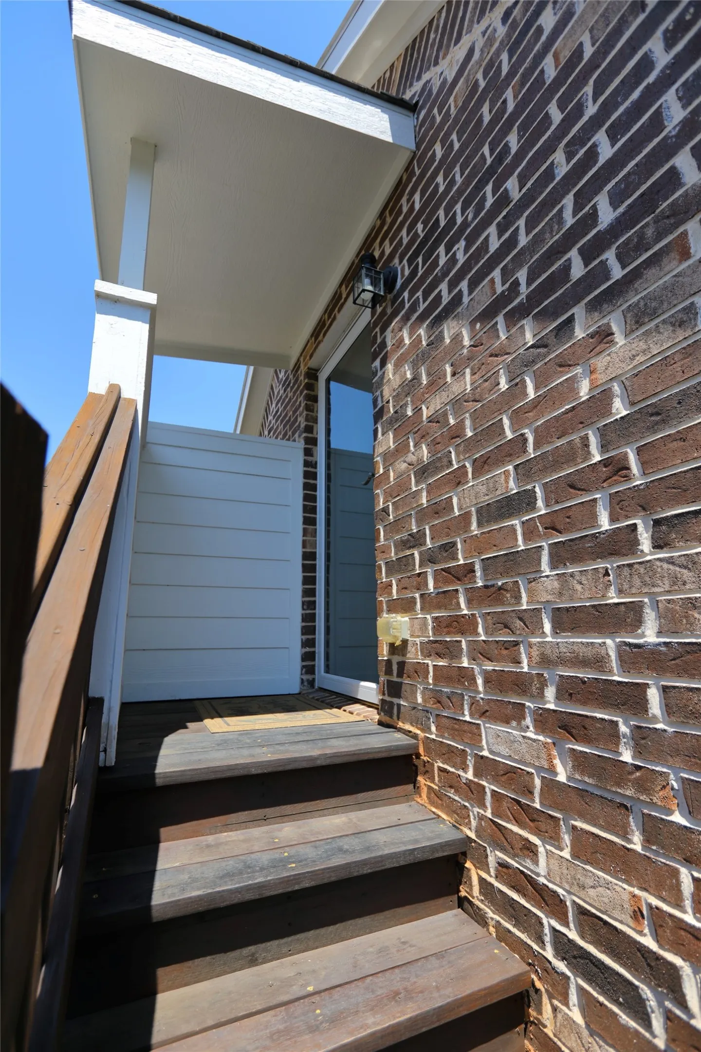 Brick exterior featuring a covered entry, dark wood-finish stairs, and a white privacy wall