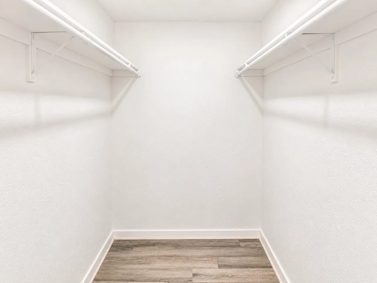 White walls, wood-finish flooring, and white shelving with hanging rods