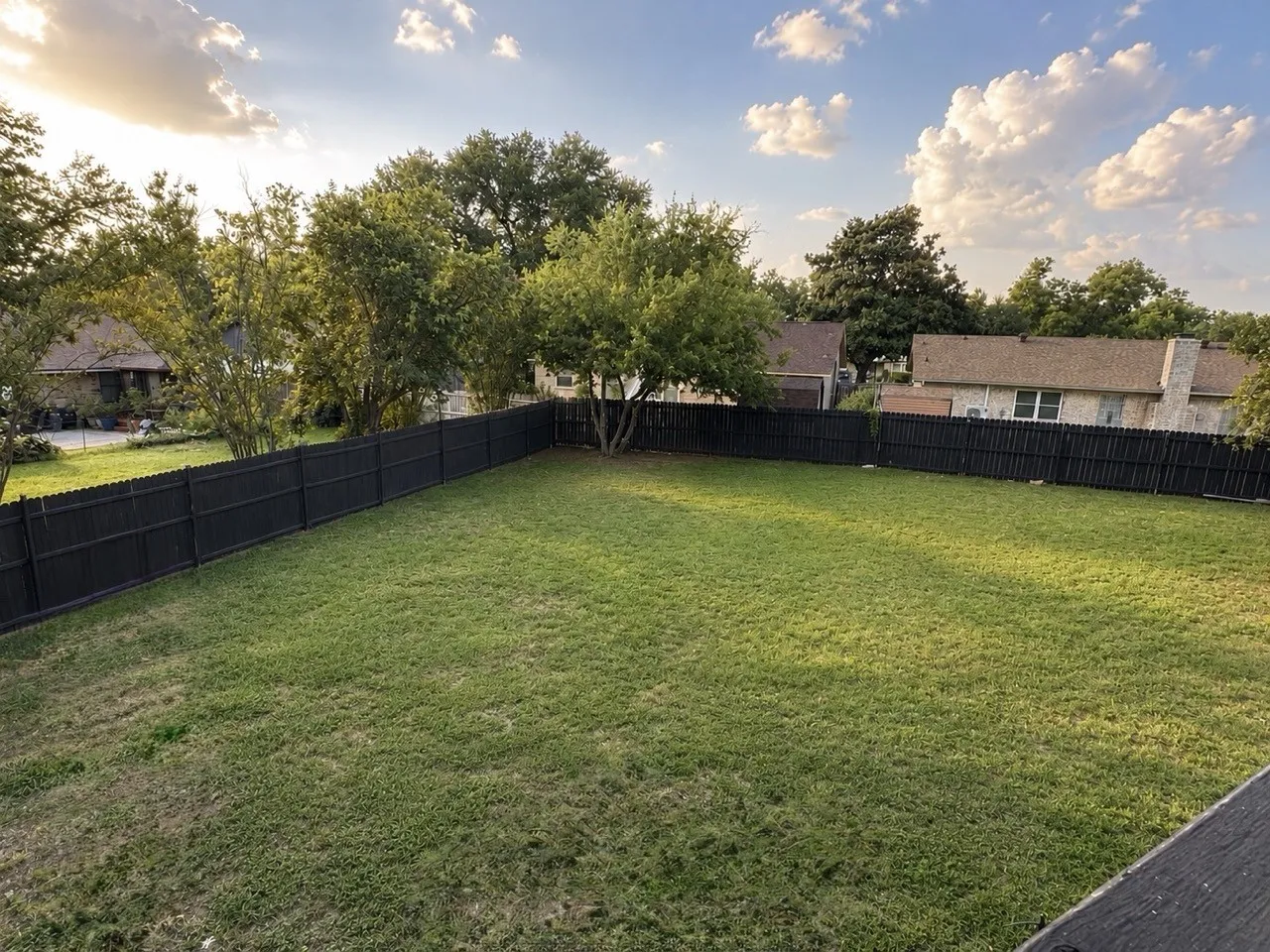 Expansive fenced backyard with a green lawn and mature perimeter trees