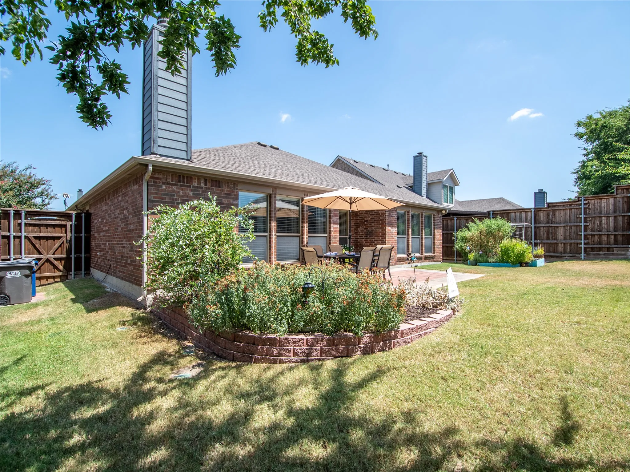 Expansive backyard featuring a brick exterior, a paved patio, and a raised garden bed with stone-look block edging