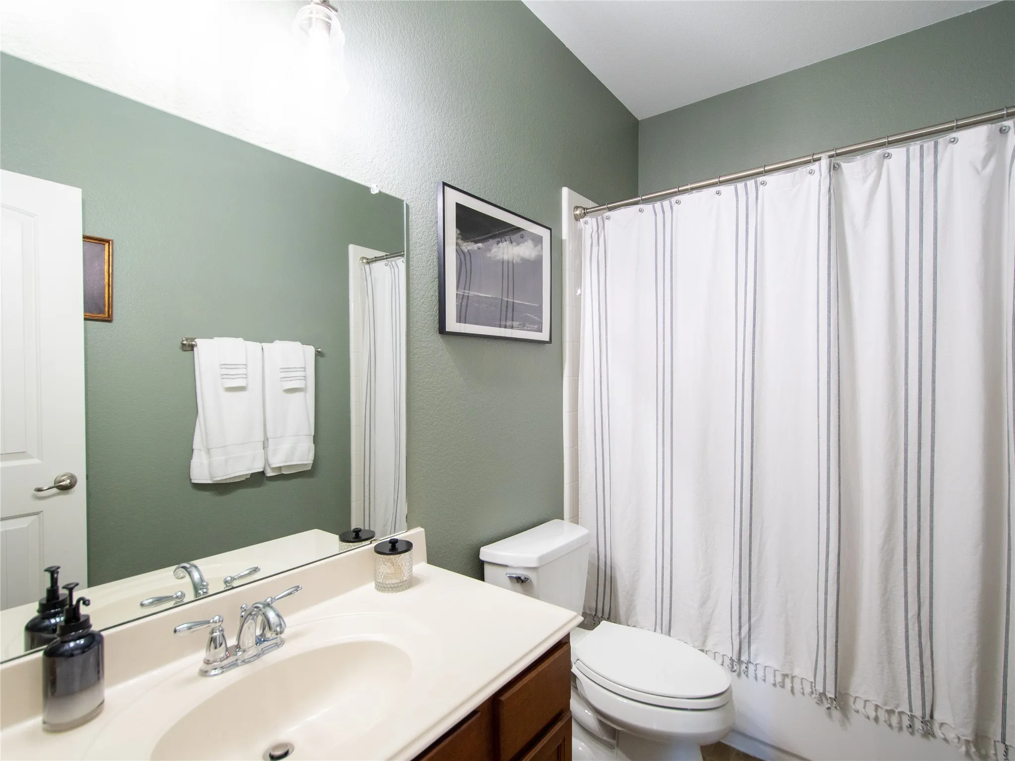 Vanity with an integrated sink and chrome faucet, large frameless mirror, and a built-in bathtub with a shower