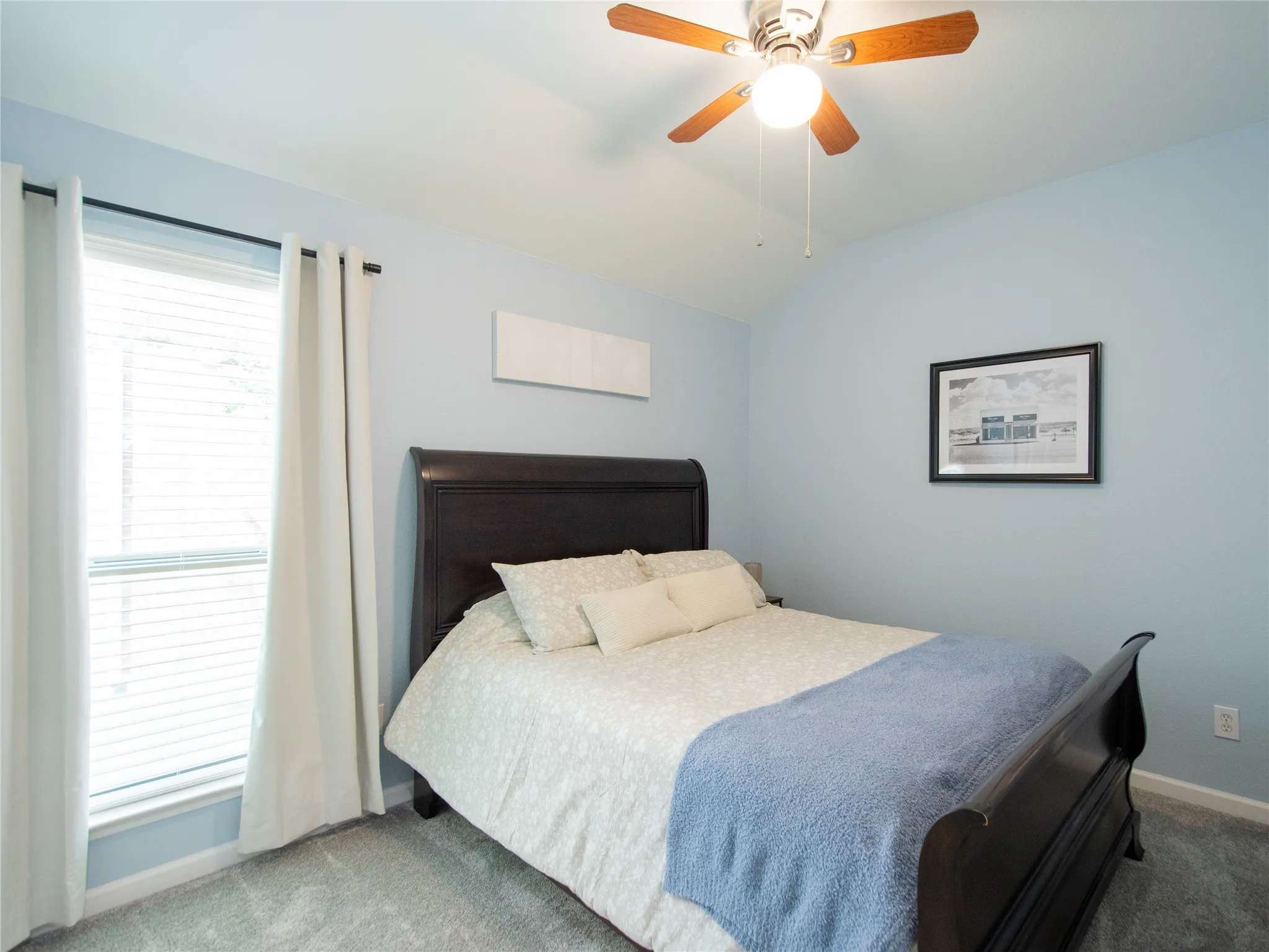 Vaulted ceiling with a ceiling fan, light blue wall paint, window with blinds, and grey carpet flooring