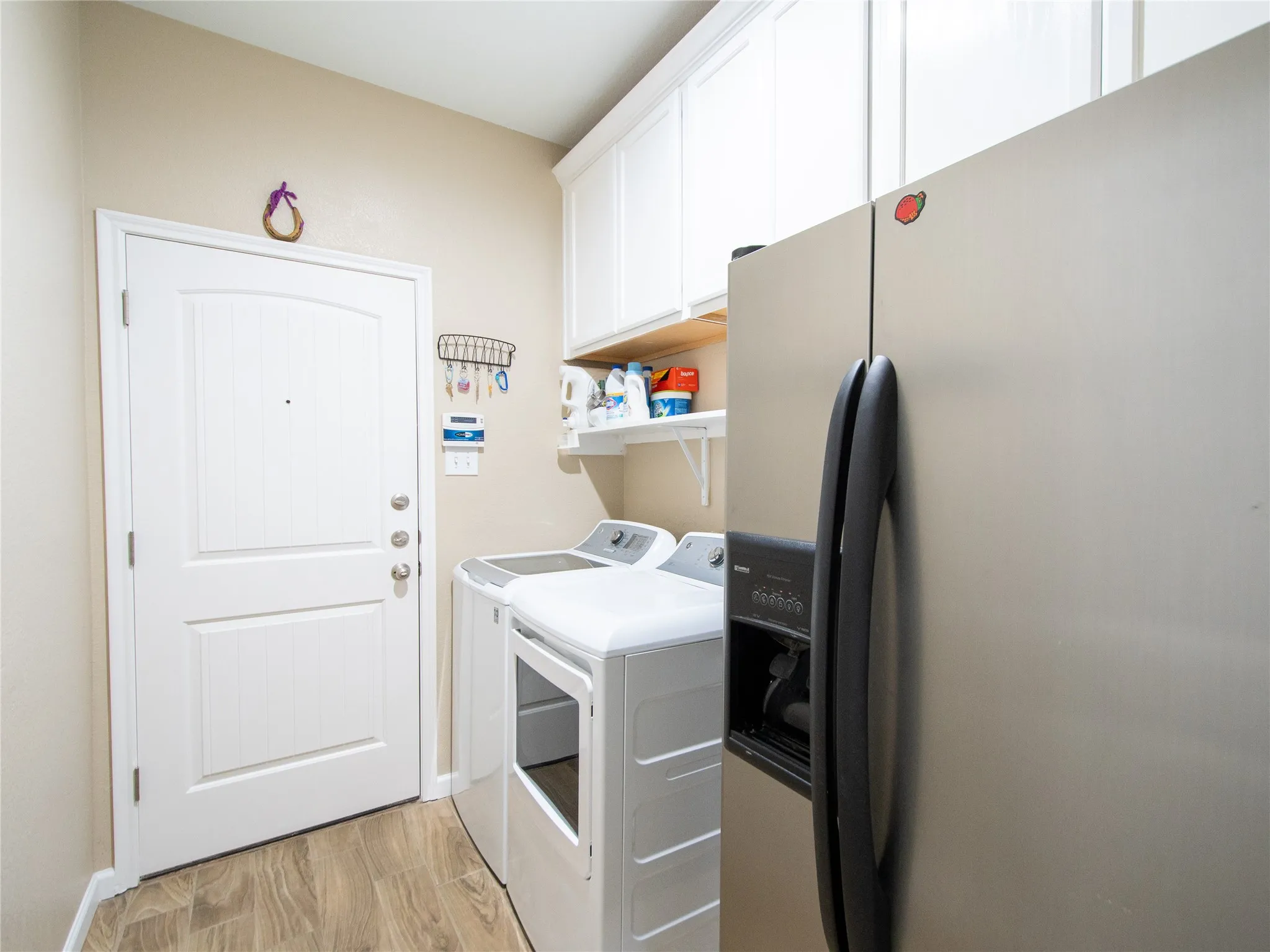 Efficient laundry room featuring stacked washer and dryer units, ample cabinetry storage, wood-finish flooring, and direct access to the home's entry