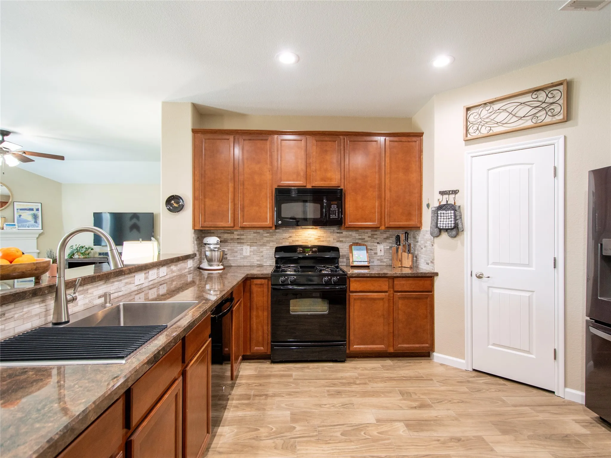 Kitchen featuring wood-finish flooring, dark wood cabinetry, a tiled backsplash, and stone-look countertops