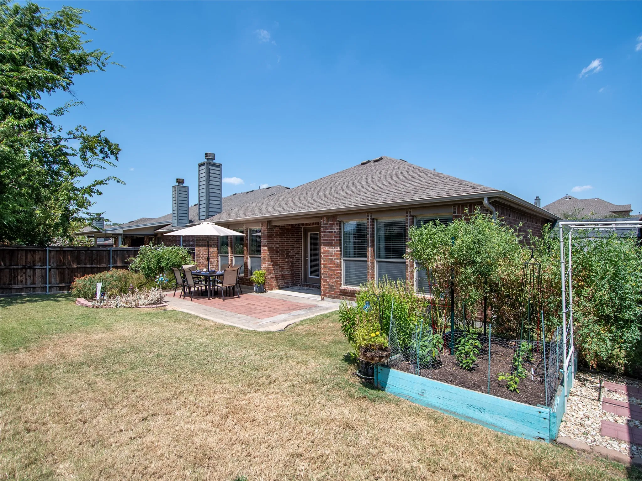 Expansive backyard featuring a brick exterior, a paver patio, mature landscaping, a garden bed, and a privacy fence