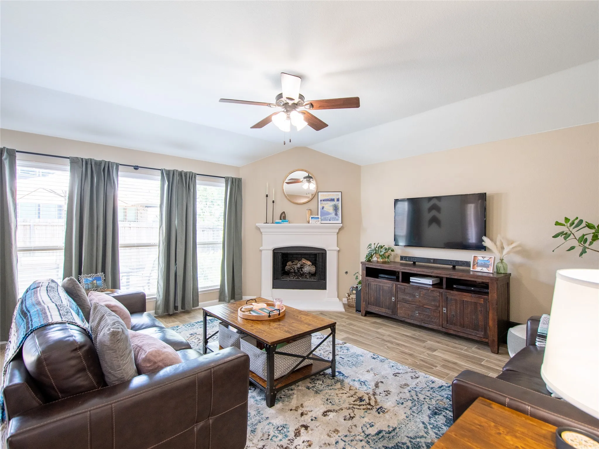 Vaulted ceiling, wood-finish flooring, ceiling fan, fireplace with mantel, and multiple windows