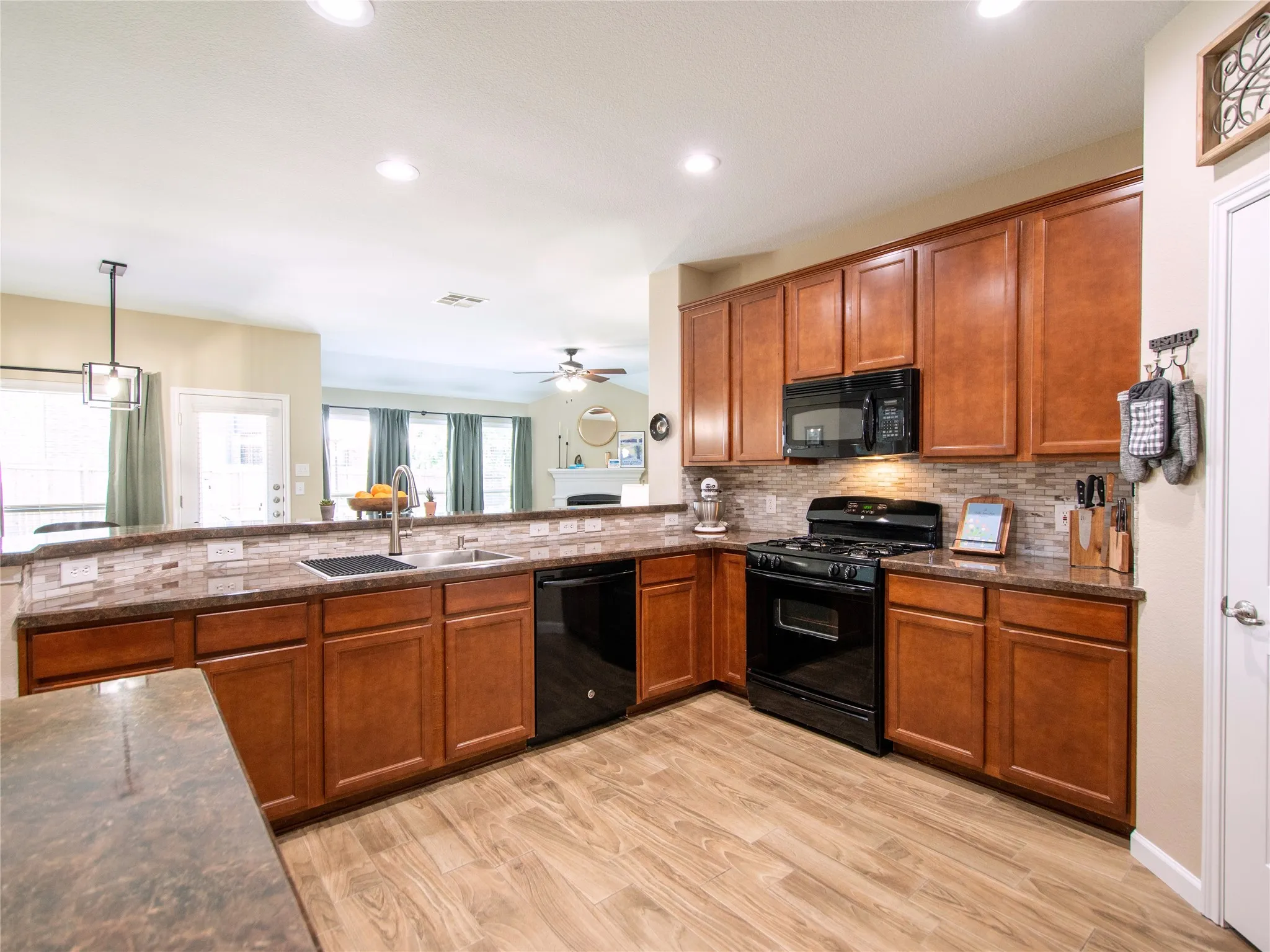 Kitchen featuring wood-finish flooring, dark wood cabinetry, black appliances, and a mosaic tile backsplash