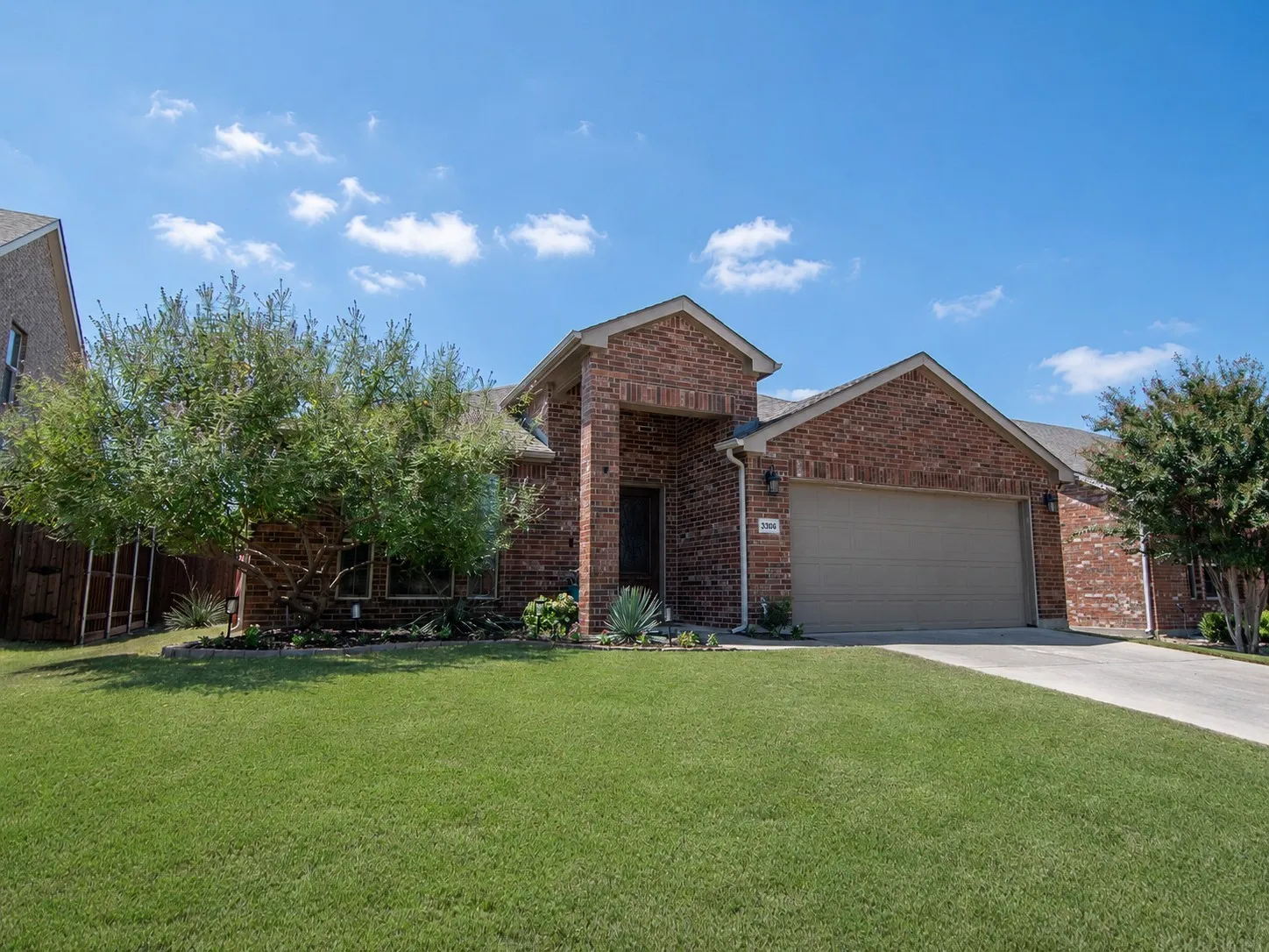 Charming brick home featuring a spacious two-car garage, manicured lawn, and mature landscaping with established trees and shrubs
