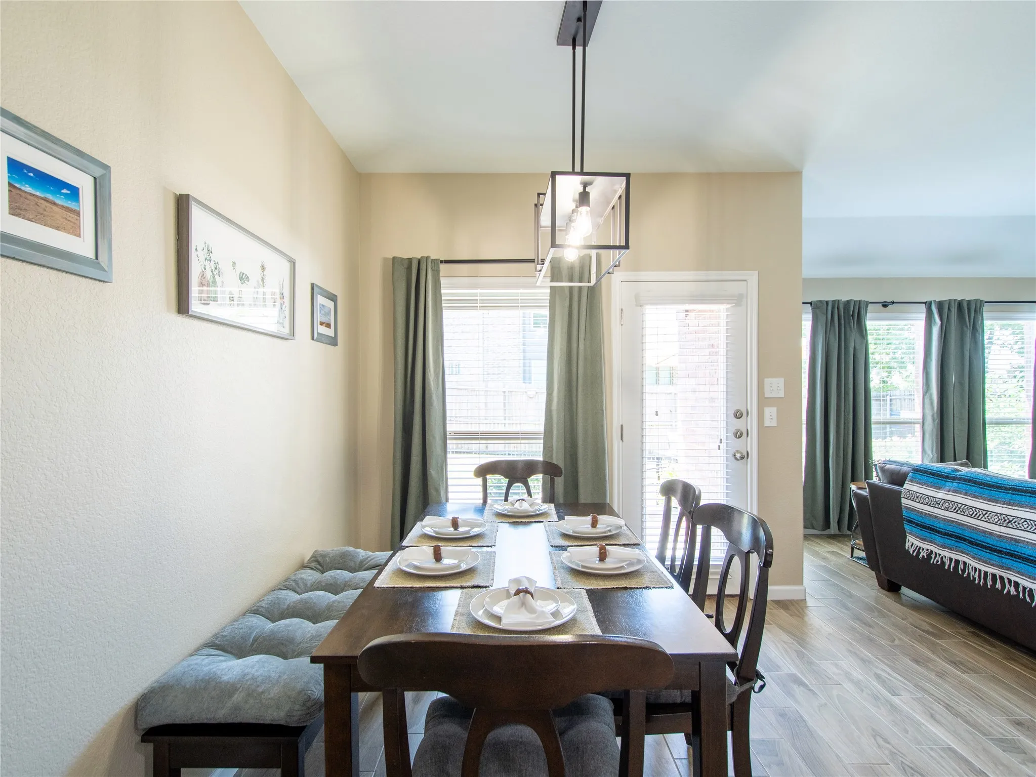 Dining area with wood-finish flooring, a contemporary pendant light fixture, and an exterior door with integrated blinds