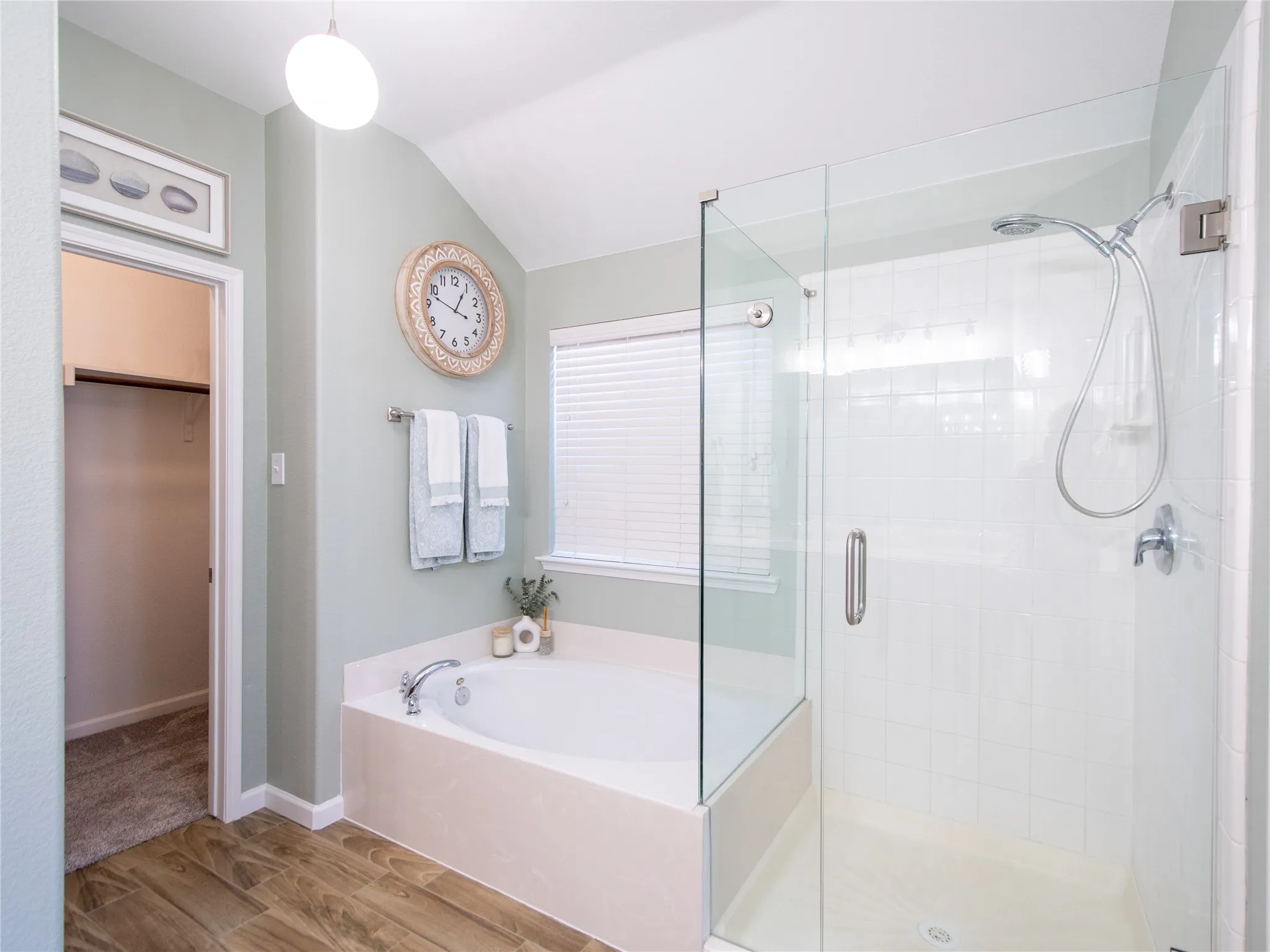Spa-inspired primary bathroom featuring a frameless glass-enclosed shower with rainfall showerhead, soaking tub with tile surround, dual vanity with vessel sink, quartz countertop, and wood-finish flooring throughout