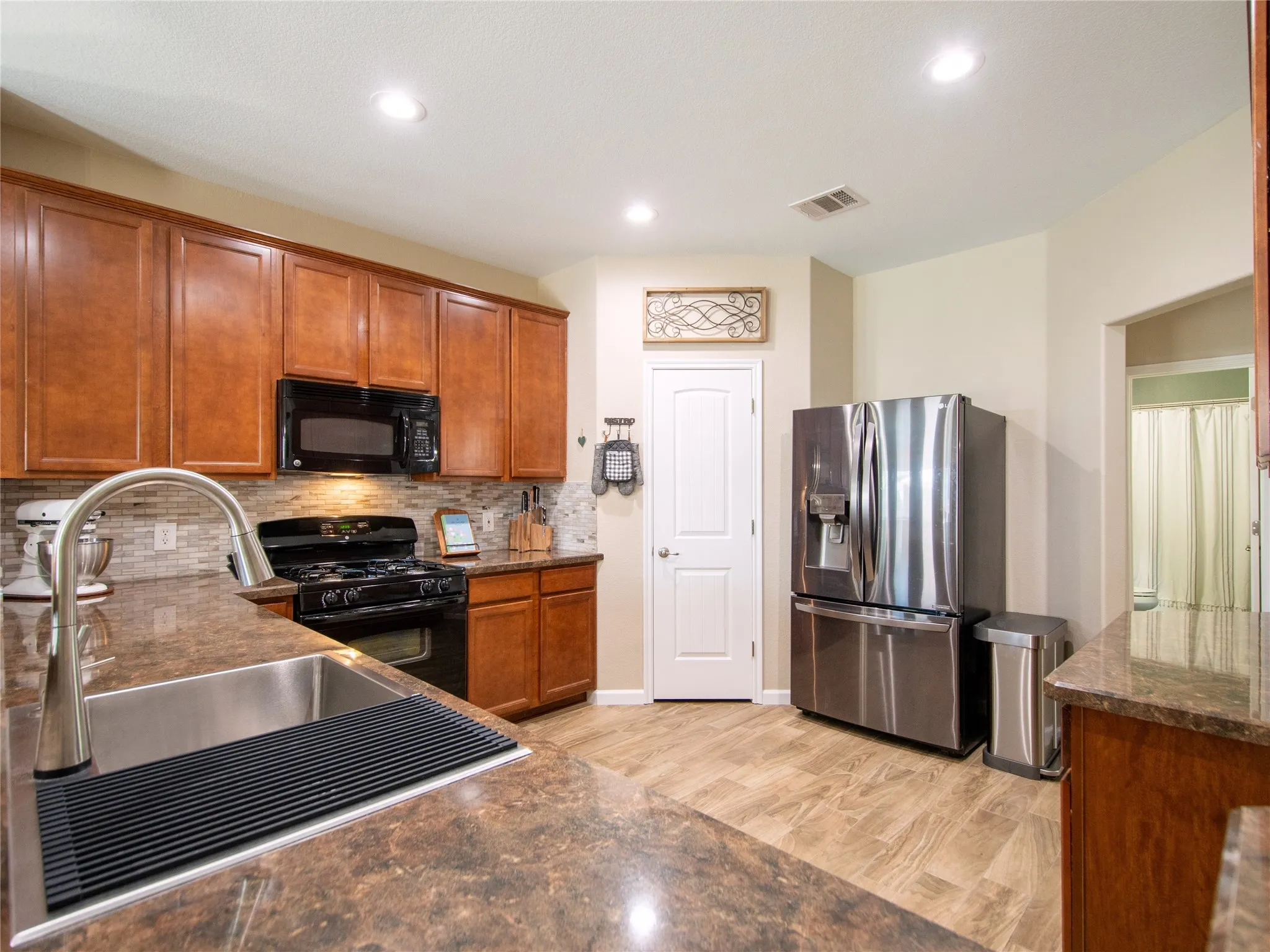 Kitchen with wood cabinetry, integrated stainless steel sink with a high-arch faucet, tile backsplash, and recessed lighting