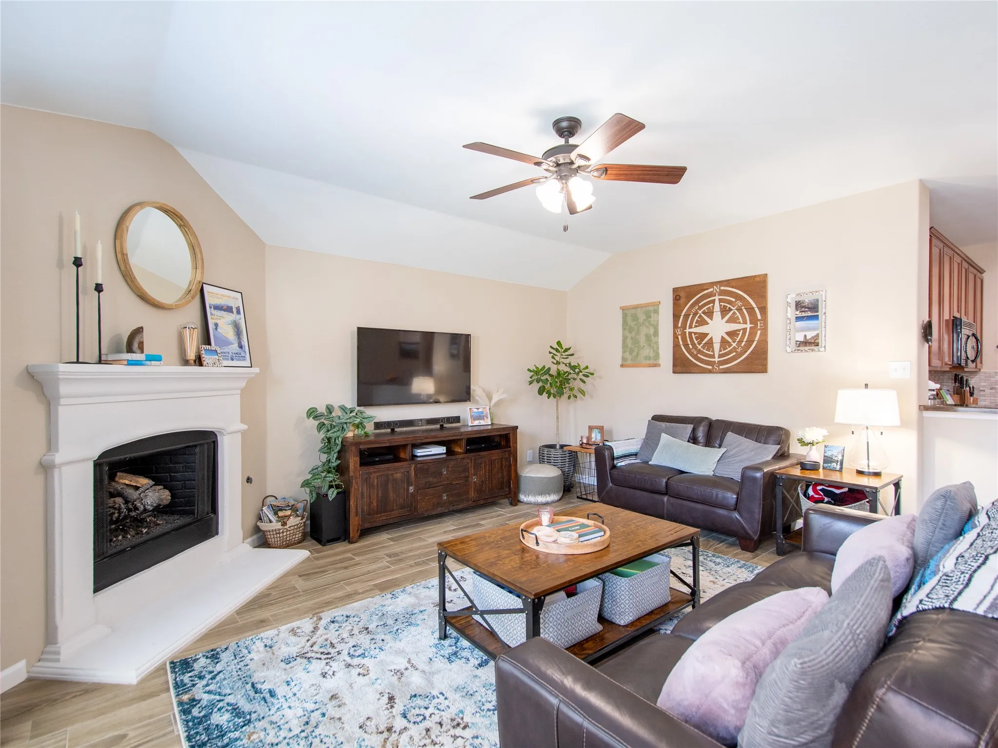 Vaulted ceiling with a ceiling fan, fireplace with a white mantel, and wood-finish flooring