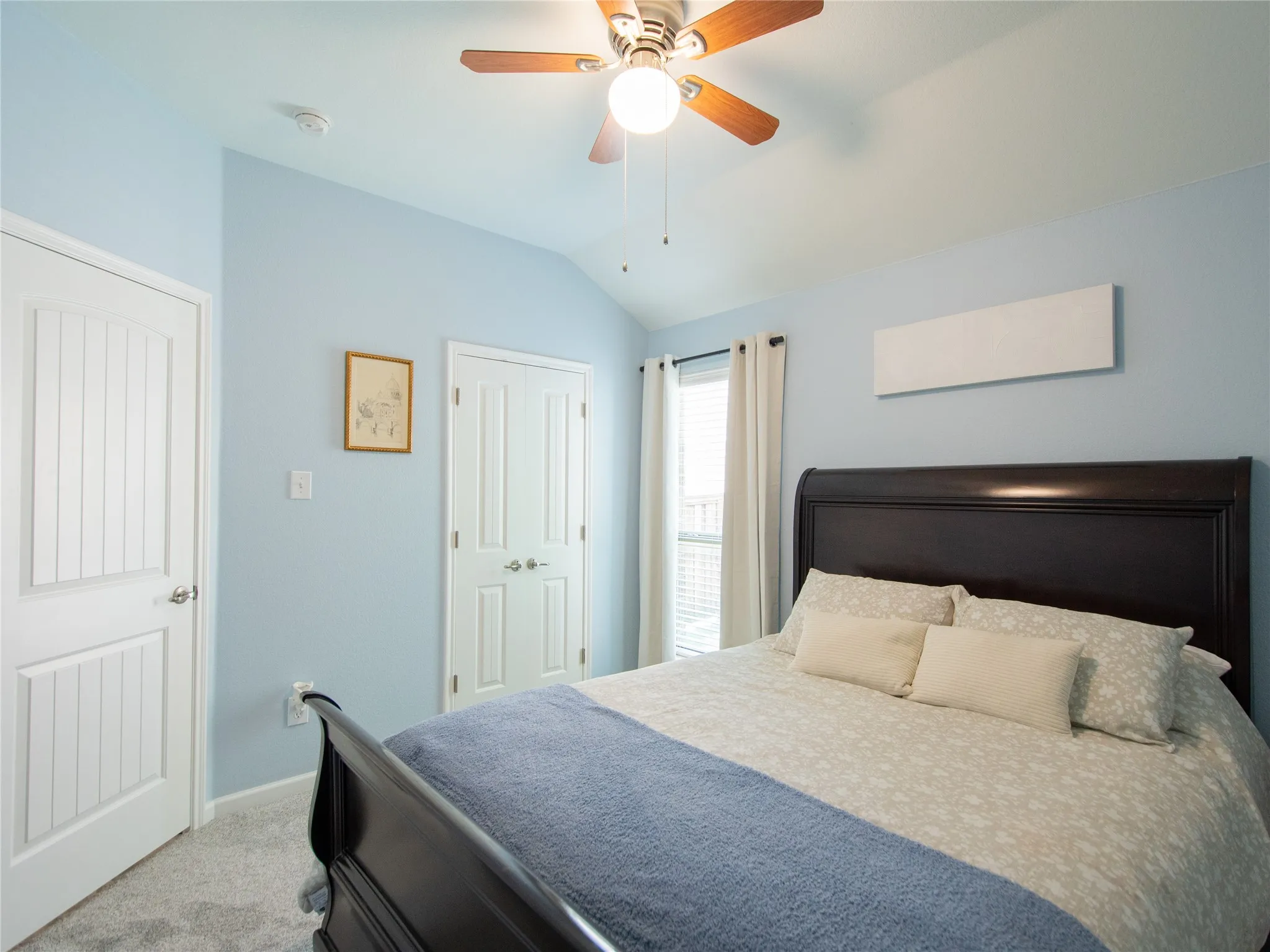 Vaulted ceiling with a ceiling fan, light blue wall paint, window with vertical blinds, white panel doors, and gray carpet