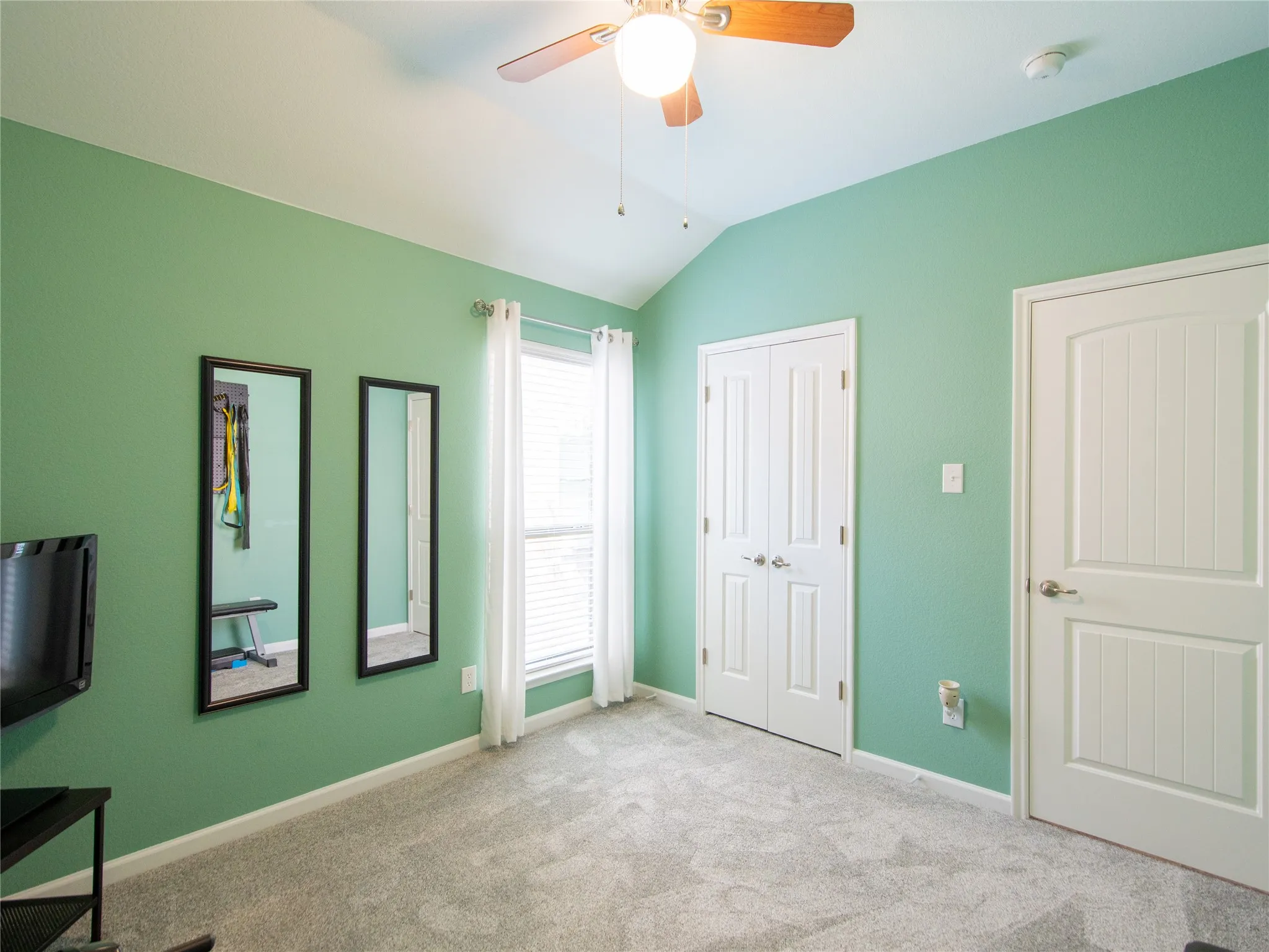 Vaulted ceiling, ceiling fan with integrated lighting, window with blinds and sheer curtains, double-door closet, paneled interior door