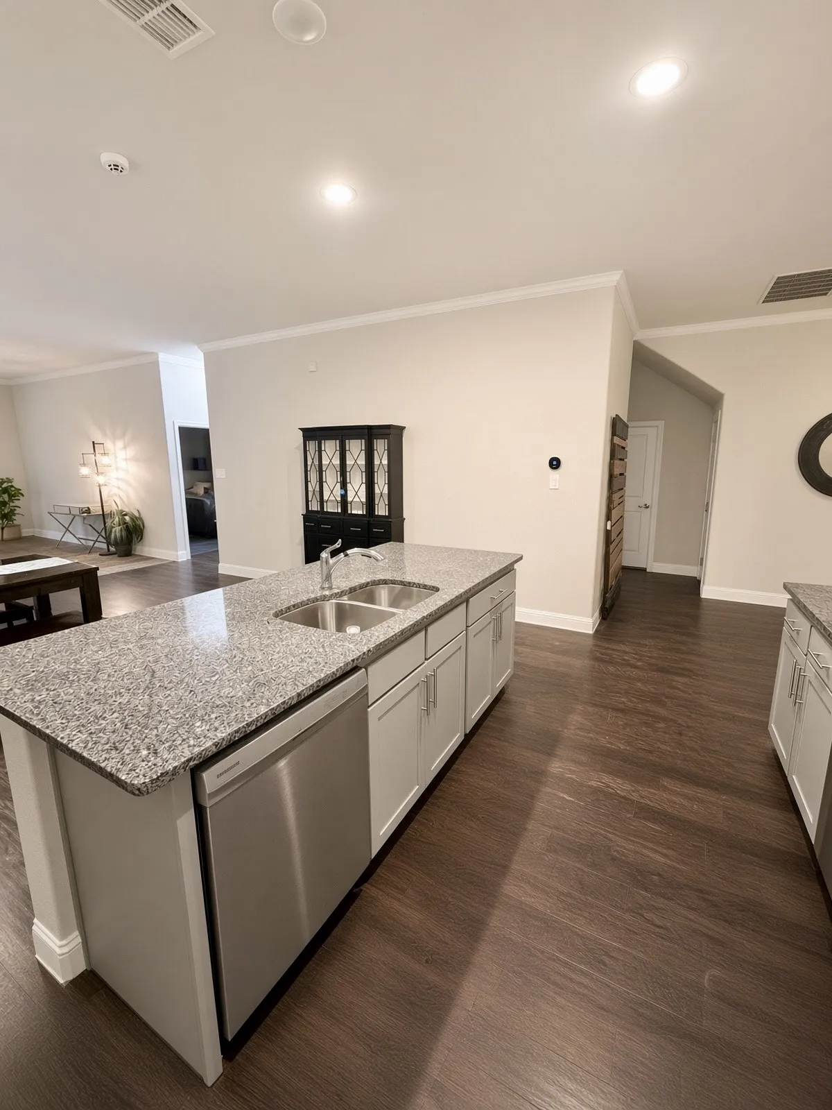Kitchen island with a dual basin sink, light grey cabinetry, and stainless steel dishwasher