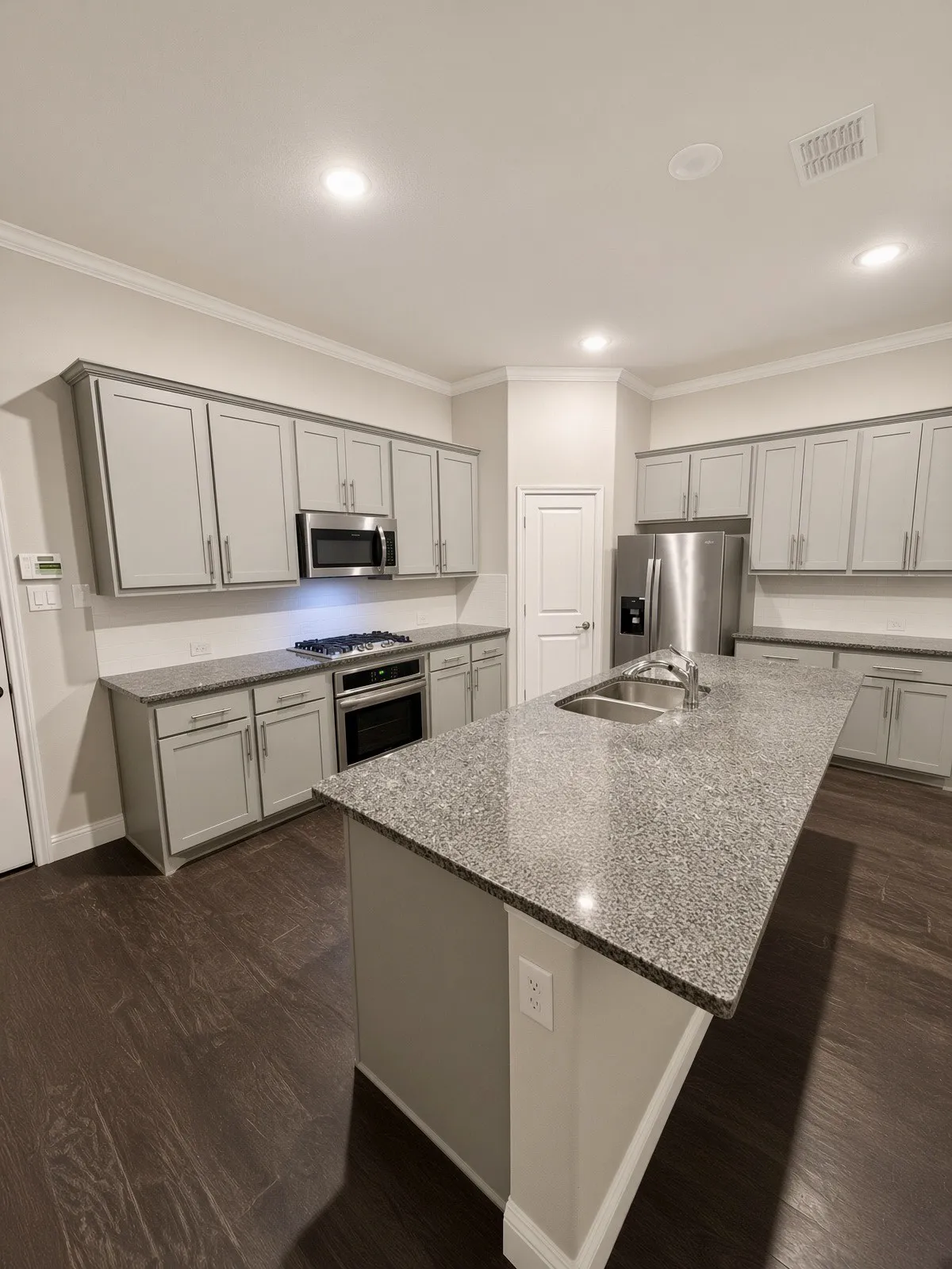 Kitchen featuring a large island with an undermount double basin sink, light-toned cabinetry, granite countertops, and wood-finish flooring