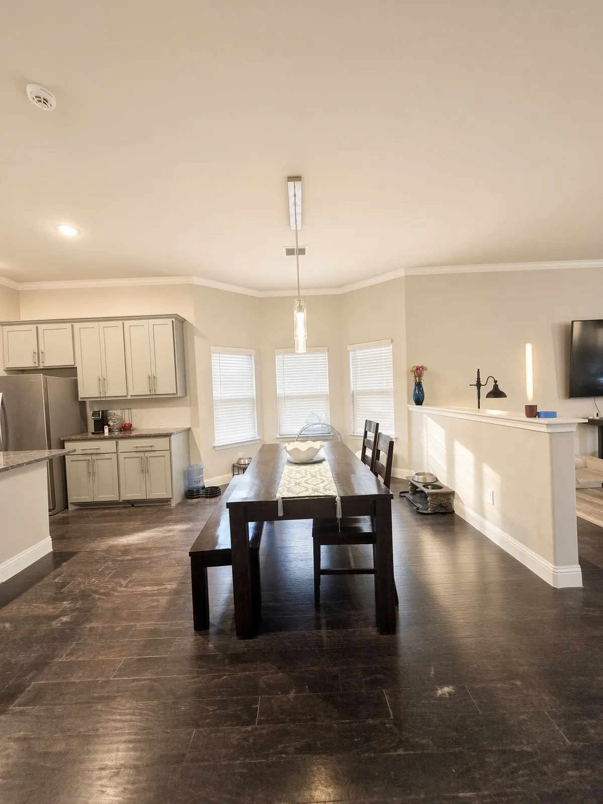 Wood-finish flooring throughout, light gray cabinetry, stainless steel appliances, and a modern pendant light fixture