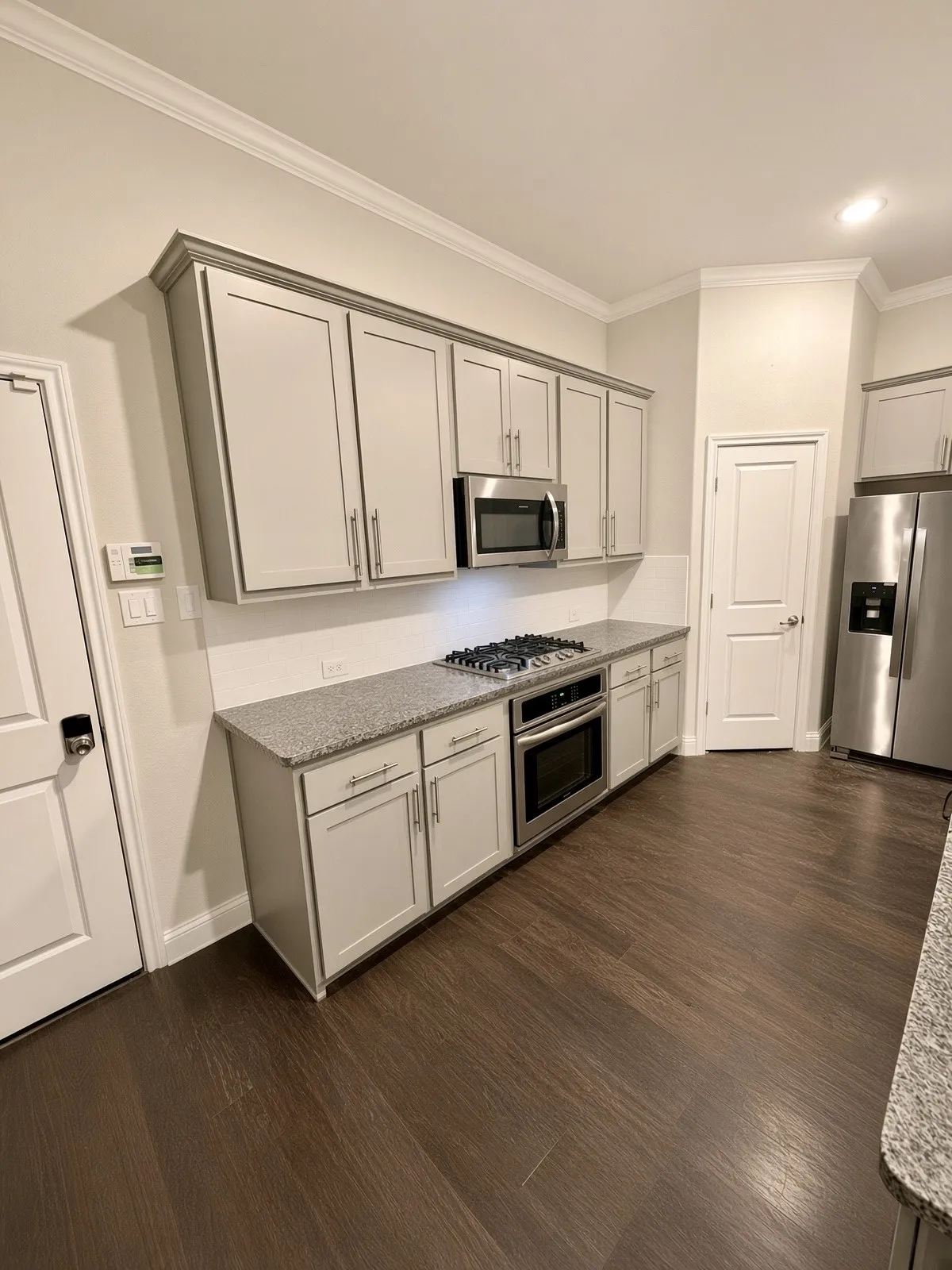 Kitchen featuring stainless steel appliances, light-toned cabinetry, granite countertops, and wood-finish flooring