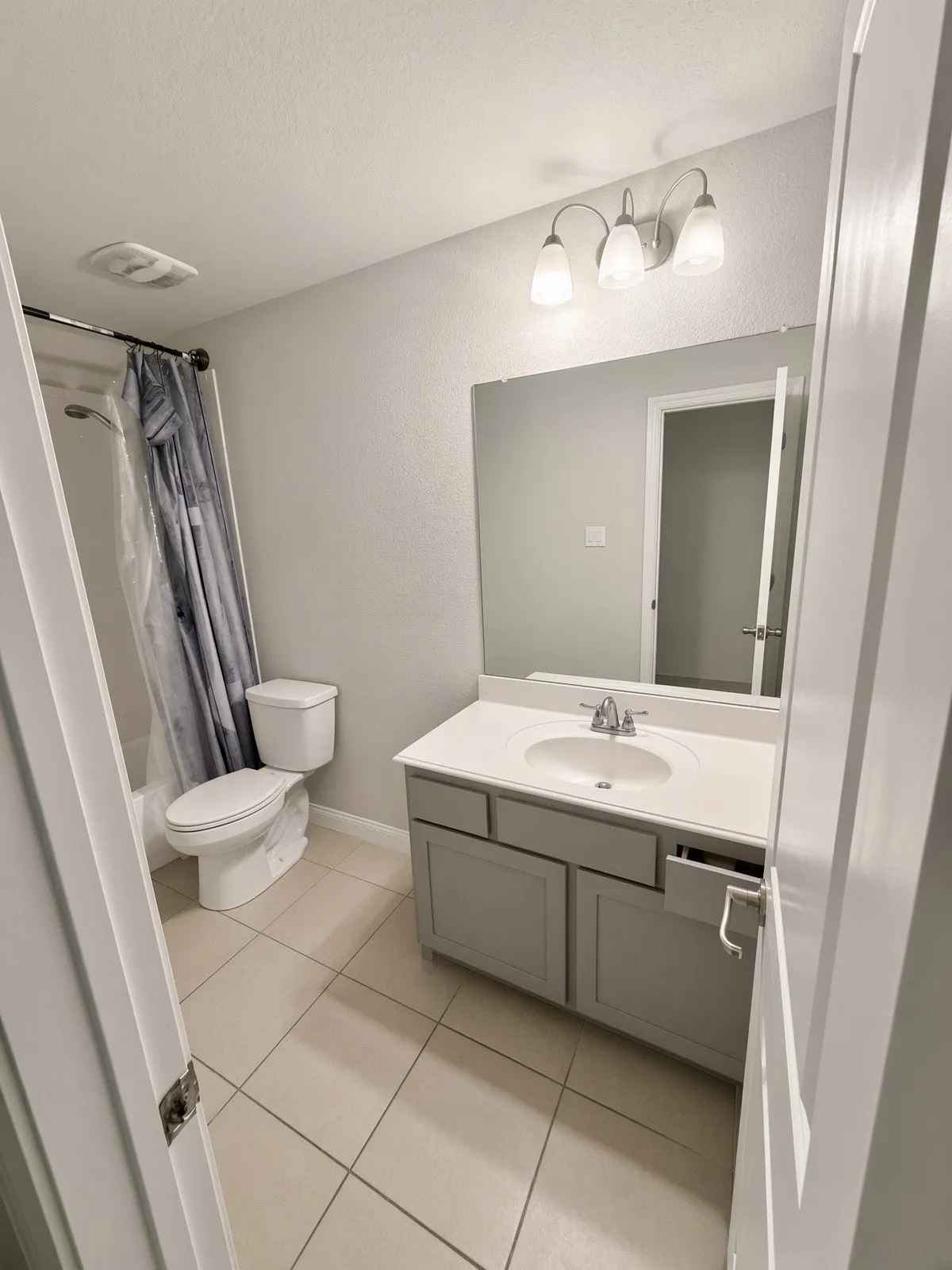 Full upstairs bathroom featuring a single vanity with a white countertop and undermount sink, a three-light vanity fixture, and a toilet with an adjacent shower and bathtub combination