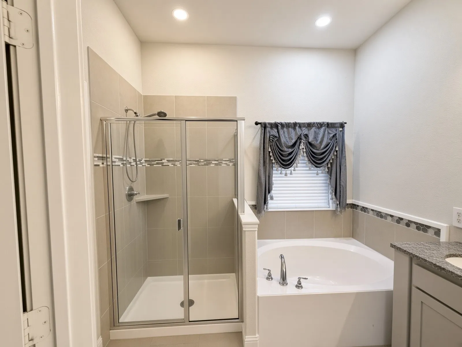 Tile shower with sliding glass door, built-in shower shelf, large soaking tub, and vanity with granite countertop