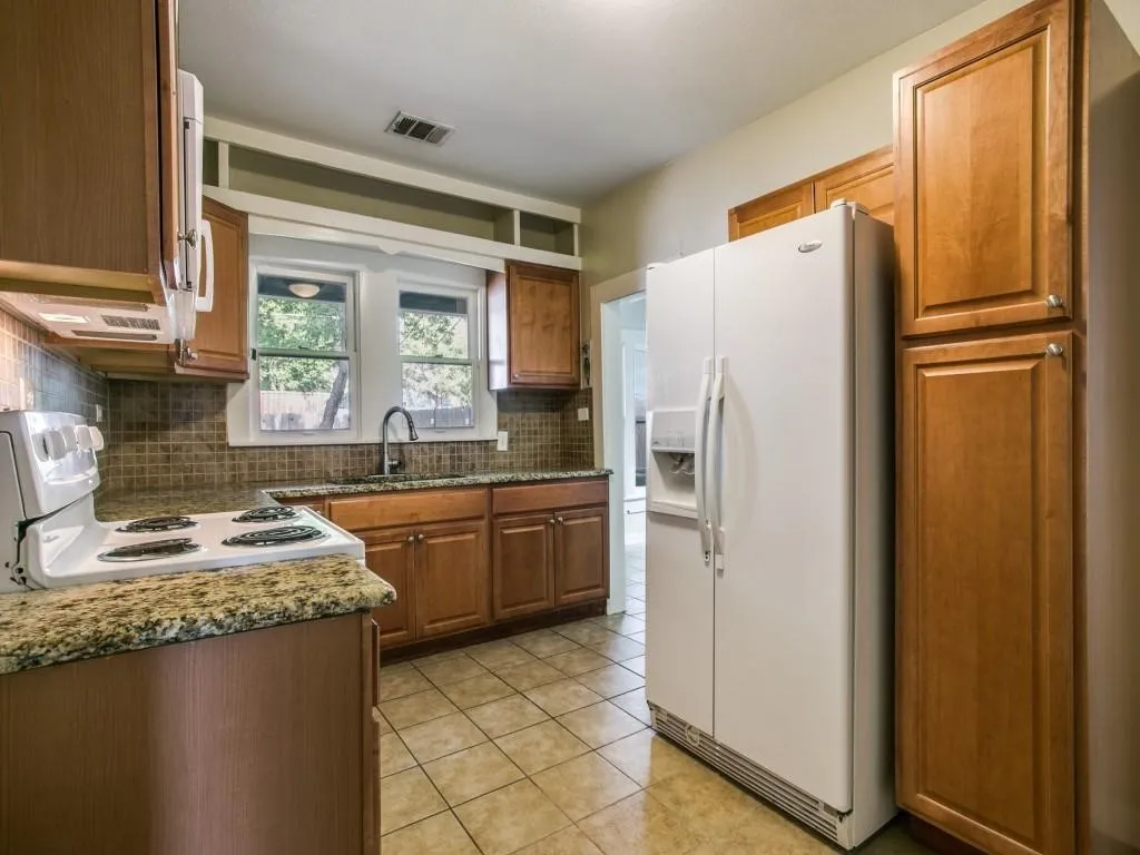 Kitchen featuring wood-finish cabinetry, granite-style countertops, mosaic tile backsplash, and ceramic tile flooring