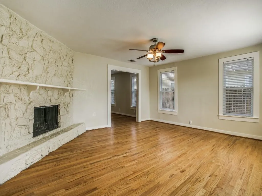 Living space featuring a stone fireplace, wood-finish flooring, and a ceiling fan with integrated lighting