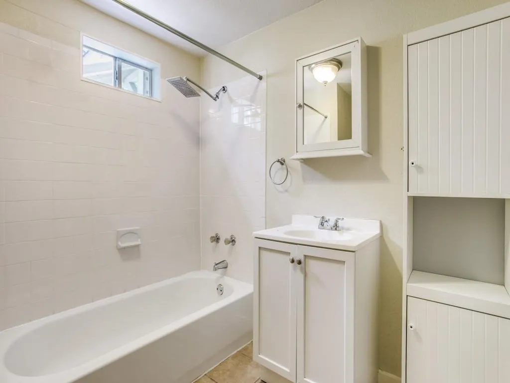 White subway tile shower surround, integrated bathtub, white vanity with cabinet storage, mirror-front medicine cabinet, and vertical slat-front storage cabinetry