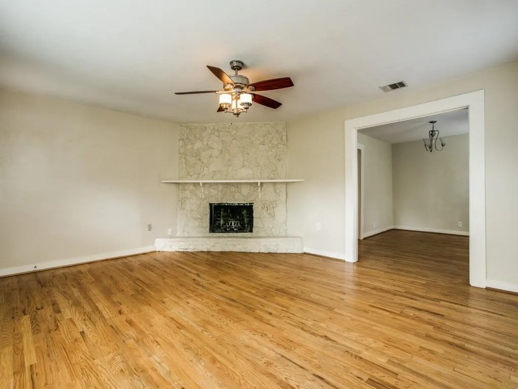 Hardwood flooring throughout, stone-clad fireplace with mantel, ceiling fan with integrated lighting, and an expansive doorway