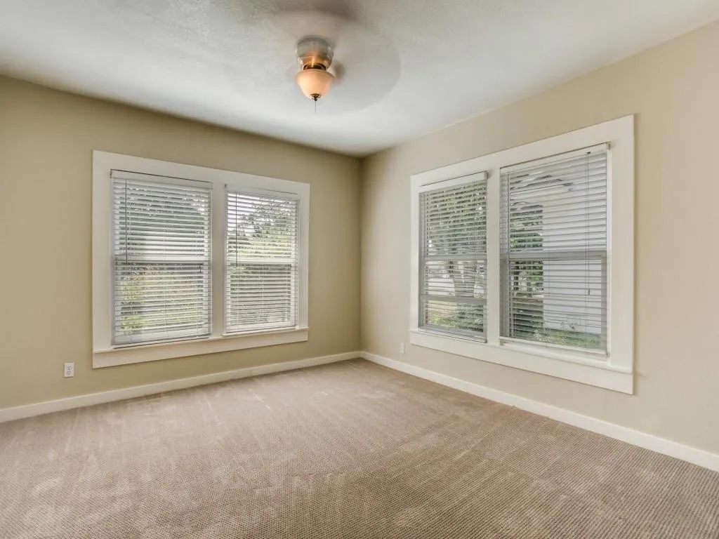 Neutral wall paint, carpet flooring, windows with blinds, and a ceiling fan